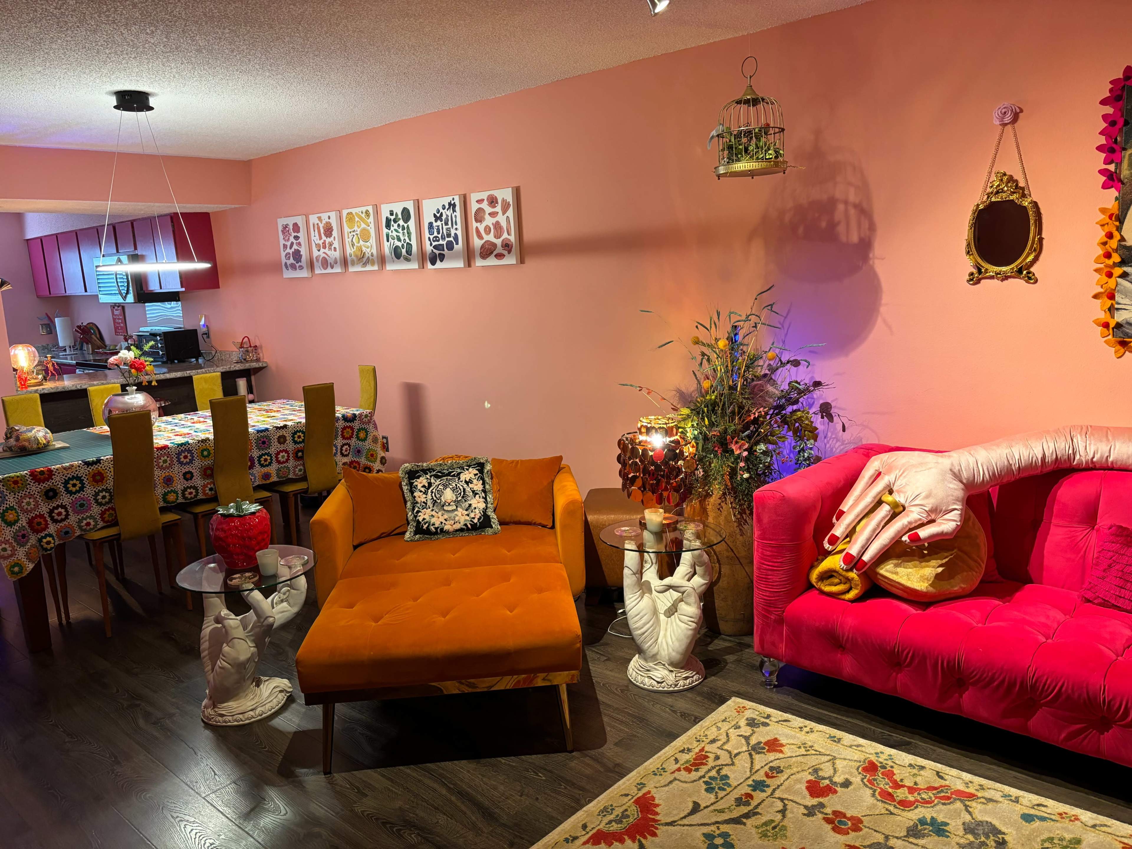 A colorful living room with two distinct sofas, a patterned tablecloth on a dining table, and artwork on the walls.