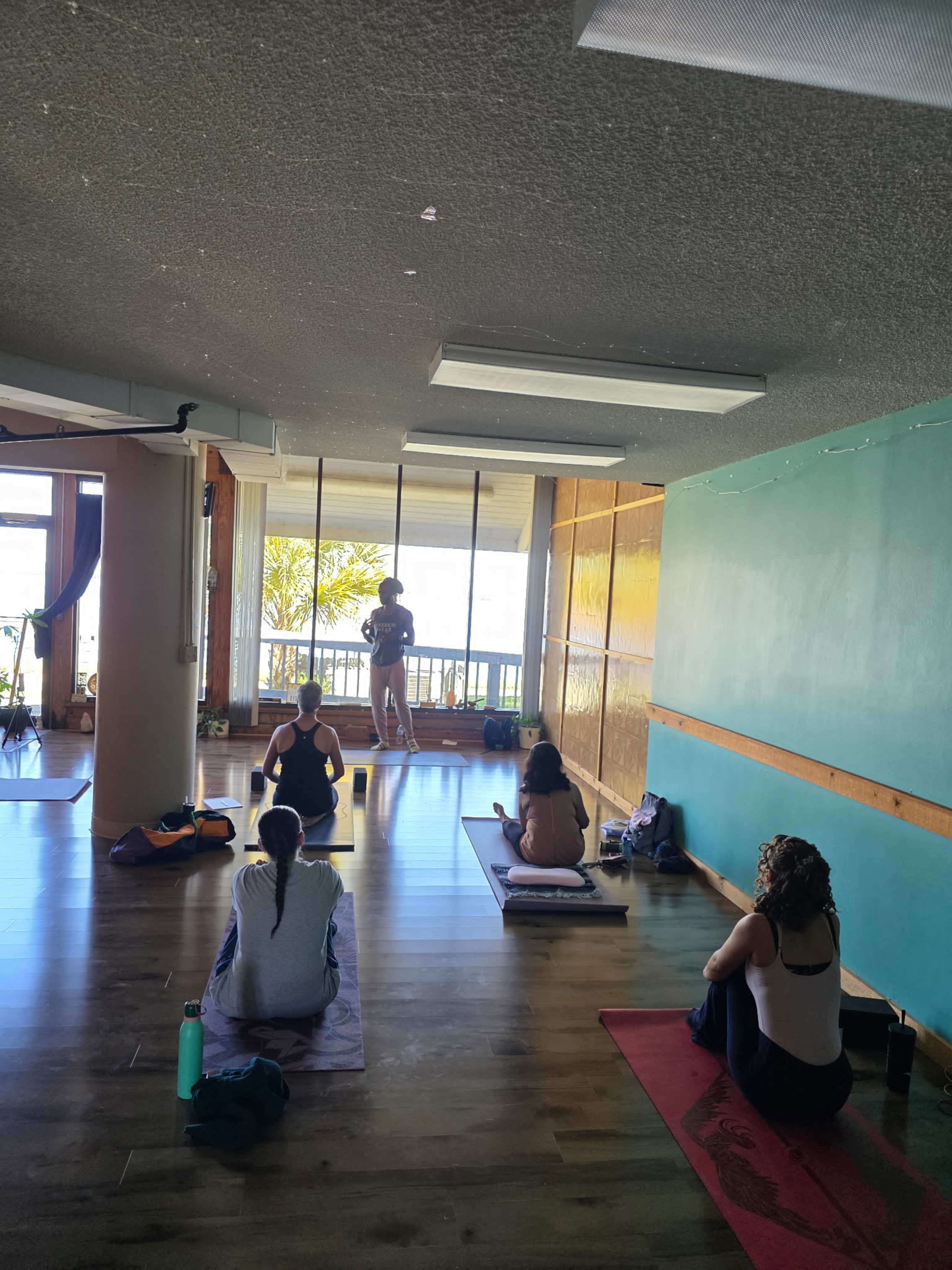 A group of people practices yoga in a studio with large windows overlooking a scenic view.