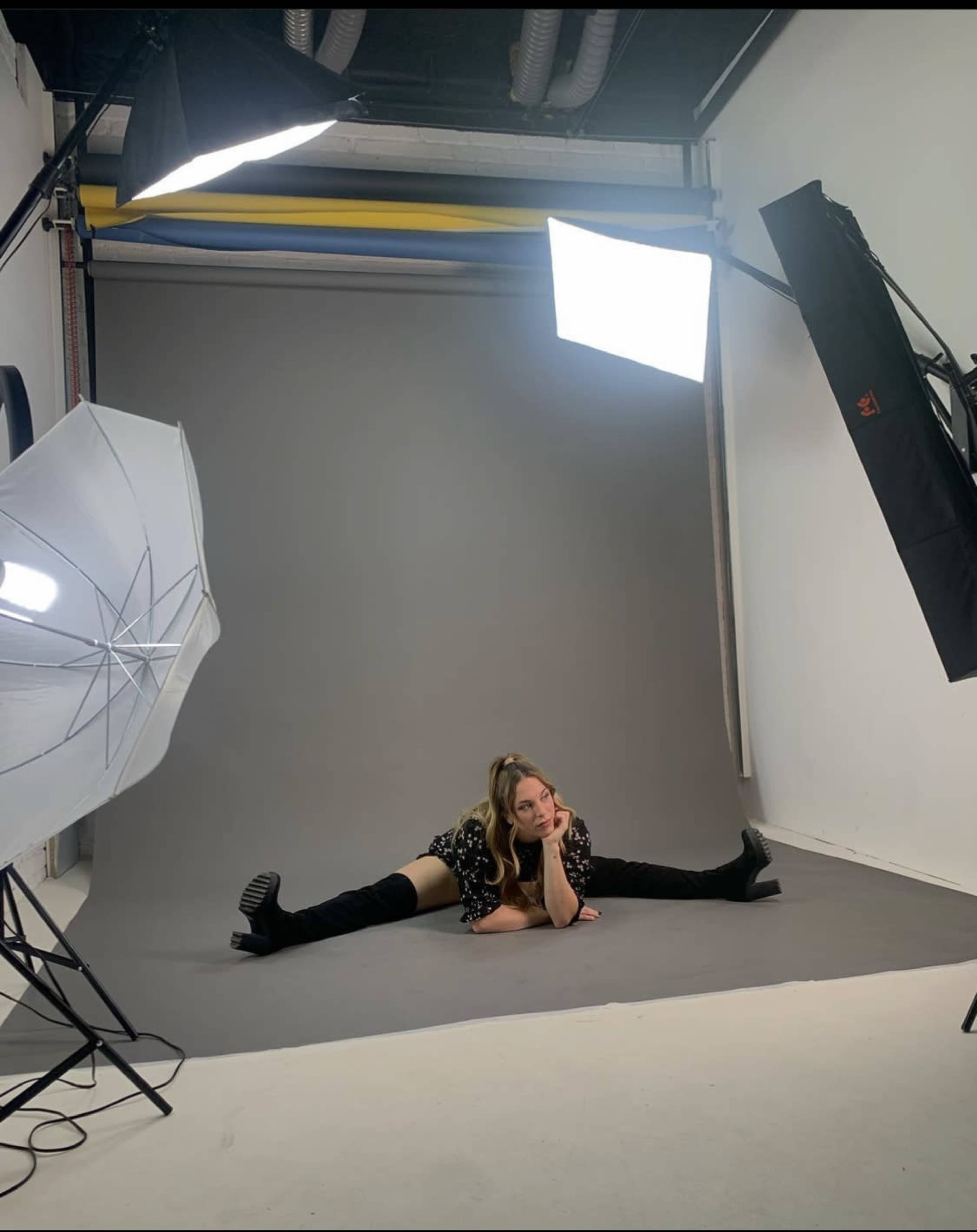 A person is posing on a gray backdrop in a photography studio with multiple lights set up around them.