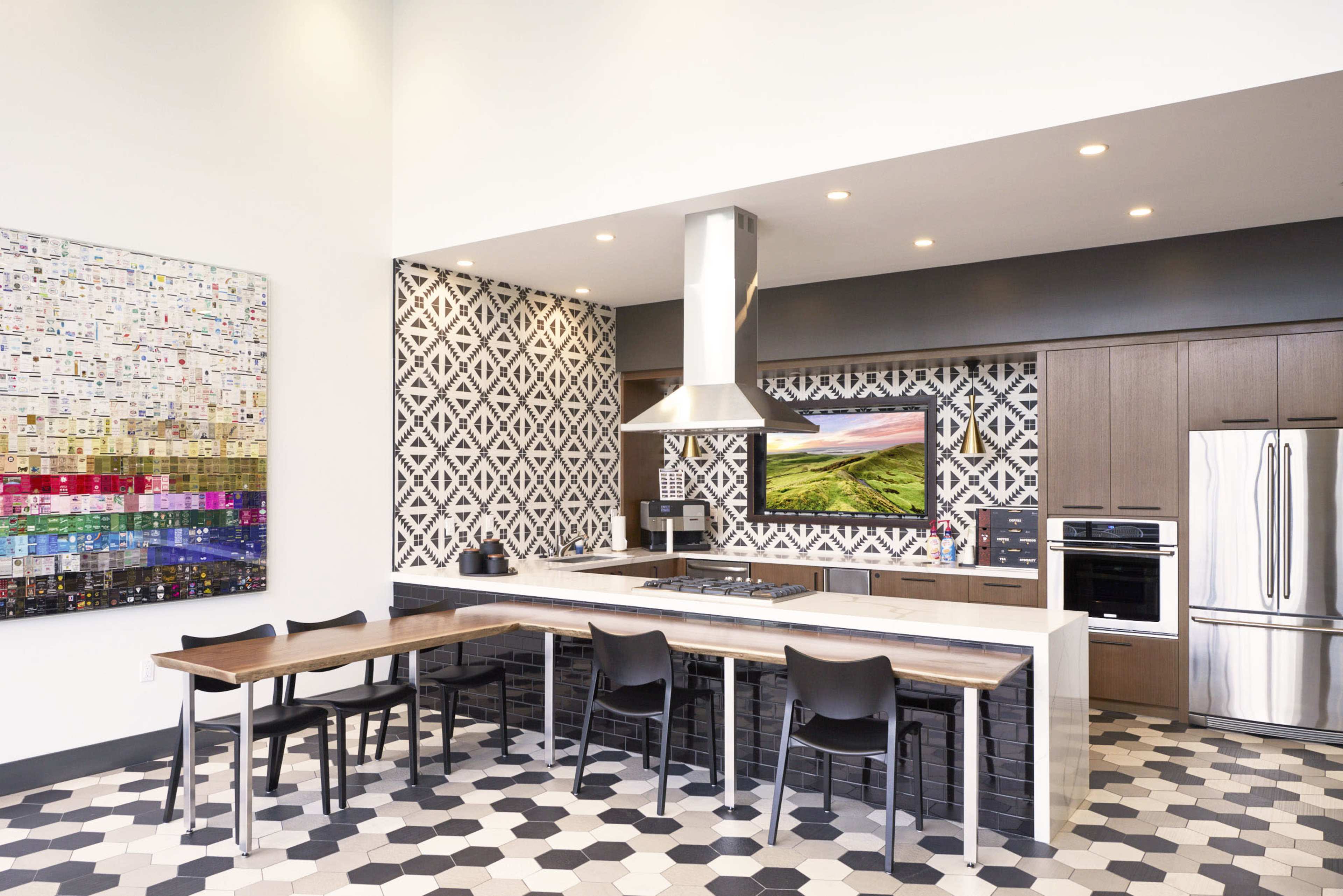 A modern kitchen featuring a large island bar with seating, a stainless steel range hood, and a geometric patterned backsplash.