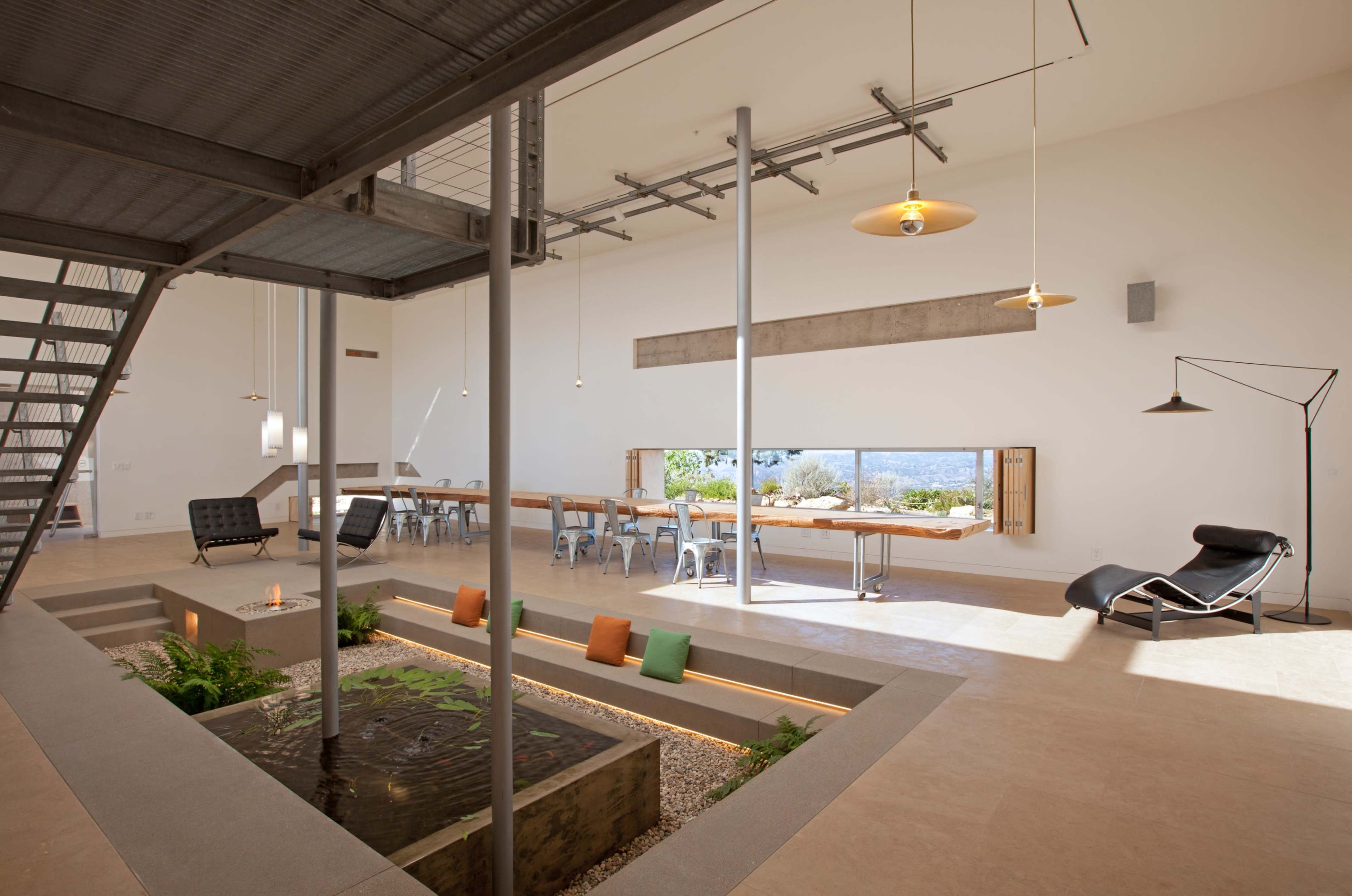 The image shows a modern interior space featuring a large window, a central indoor garden with seating, and tables arranged for dining or work.