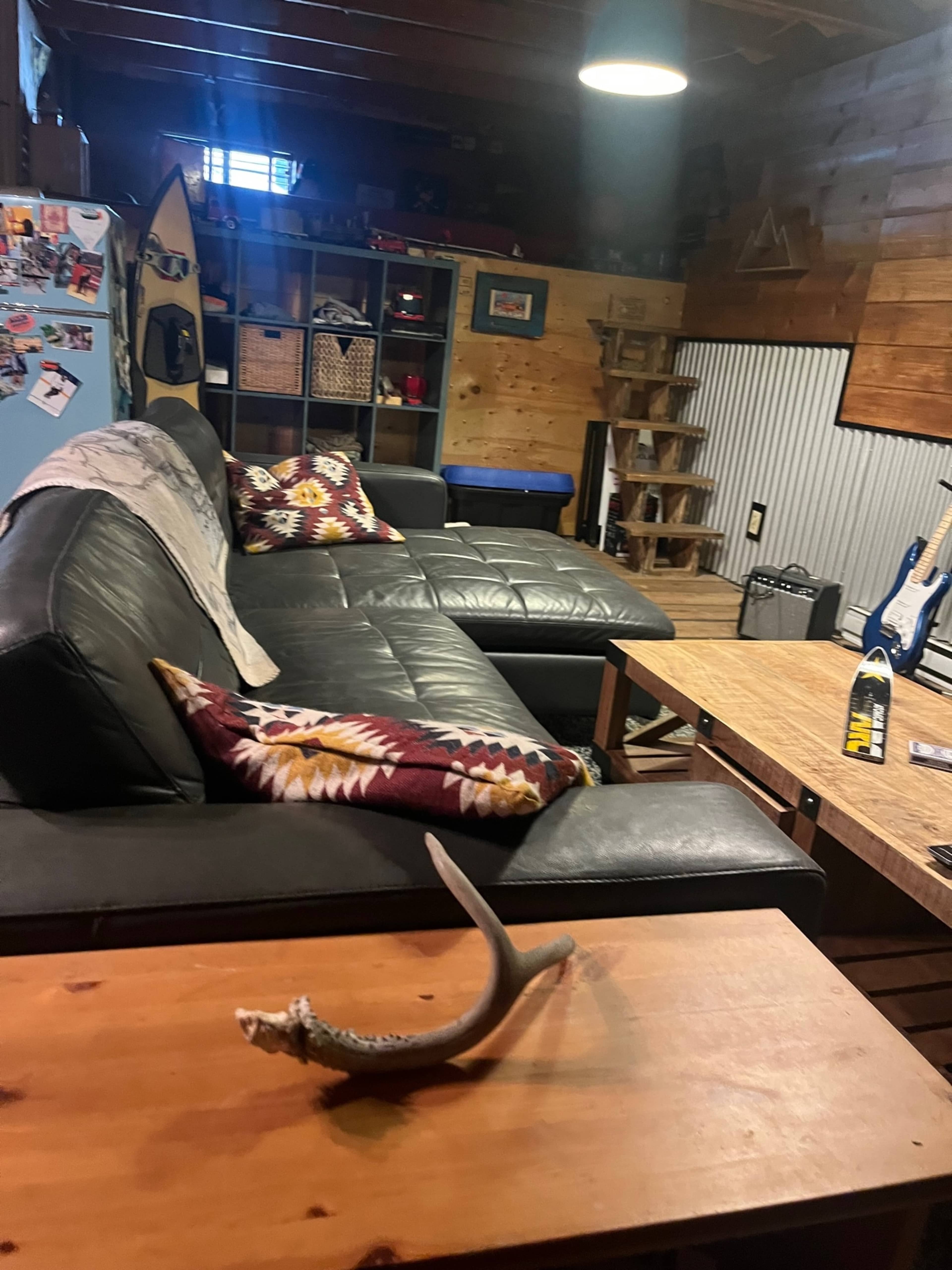 A cozy living room with a black sectional couch, a wooden coffee table, shelves, and a guitar visible in the background.