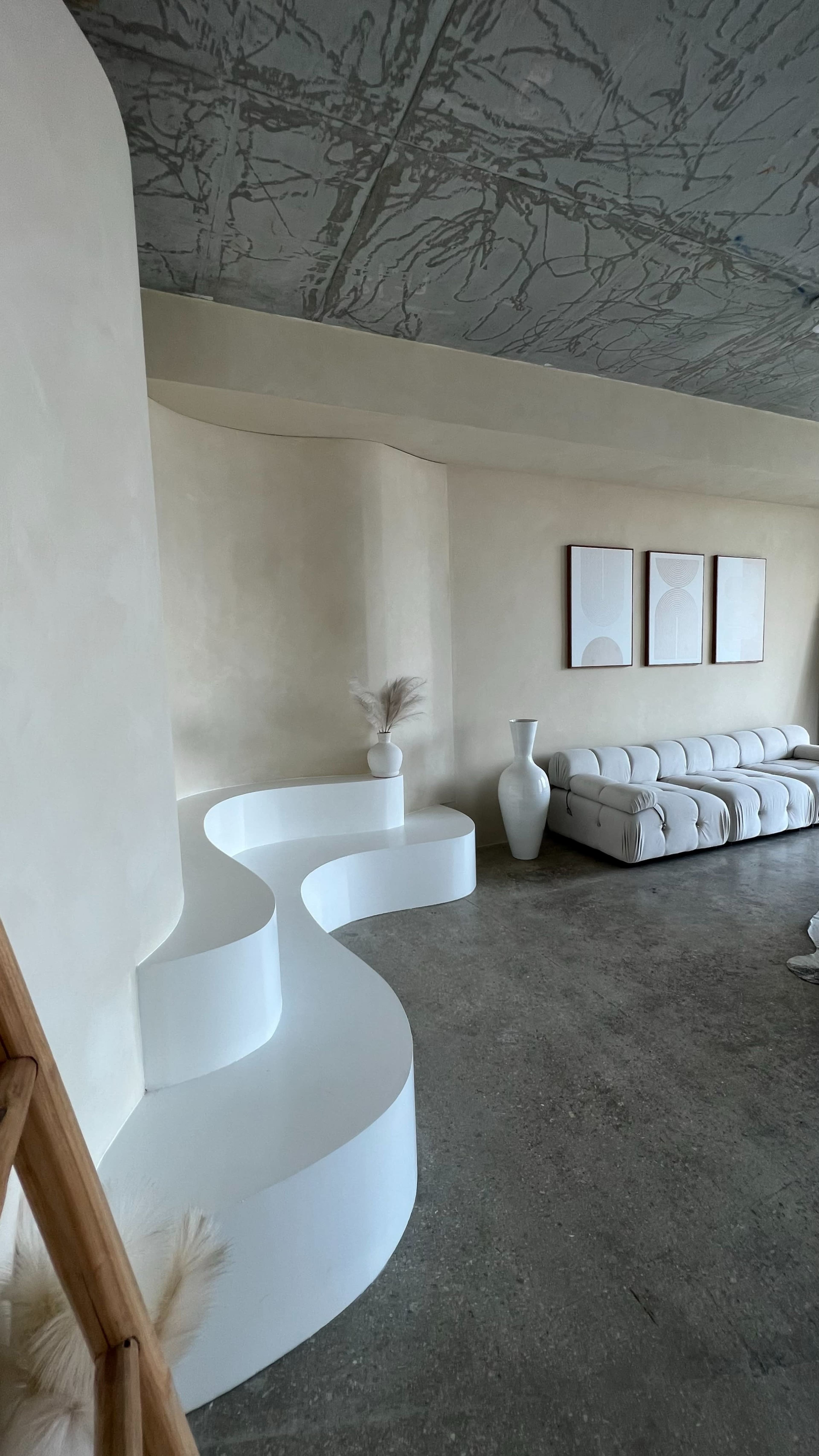 A minimalistic living room featuring a curved white seating area, a white vase, and three framed artworks on the wall.