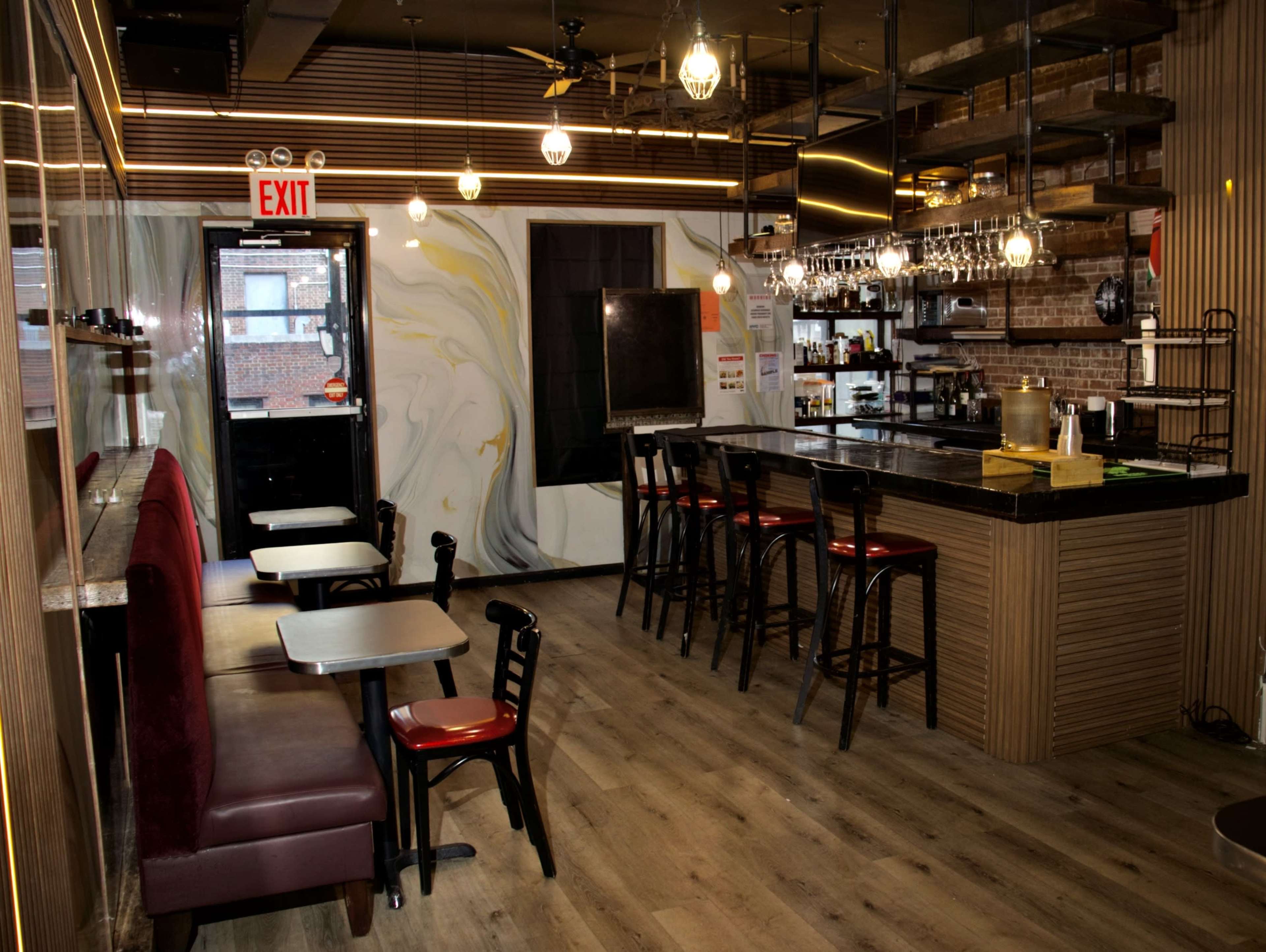The image shows a modern café interior with a bar area, tables, and seating along the walls, featuring a mix of wooden floors and stylish lighting fixtures.