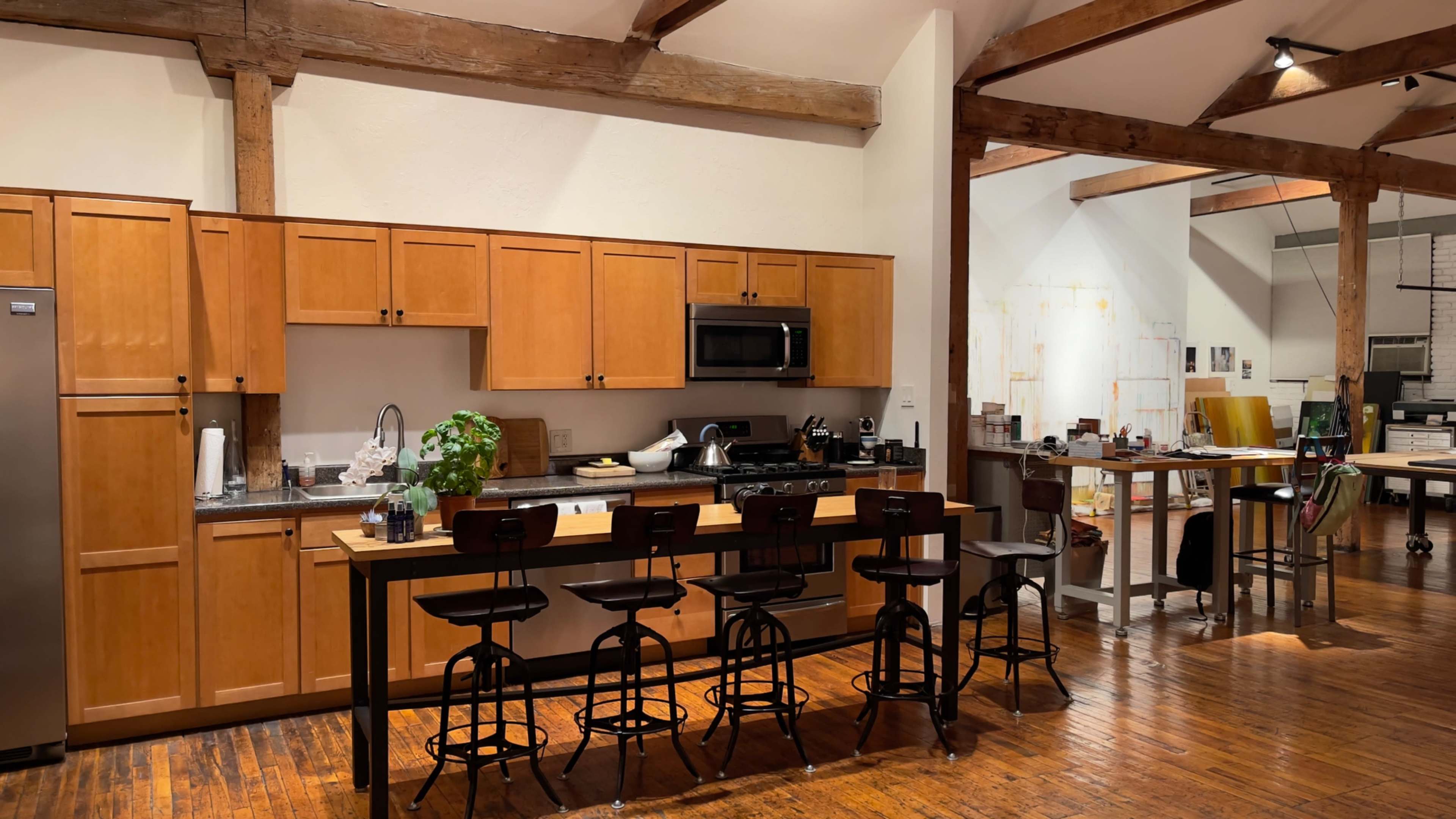 The image shows a spacious kitchen with wooden cabinetry, a central island with bar stools, and exposed wooden beams in the ceiling.