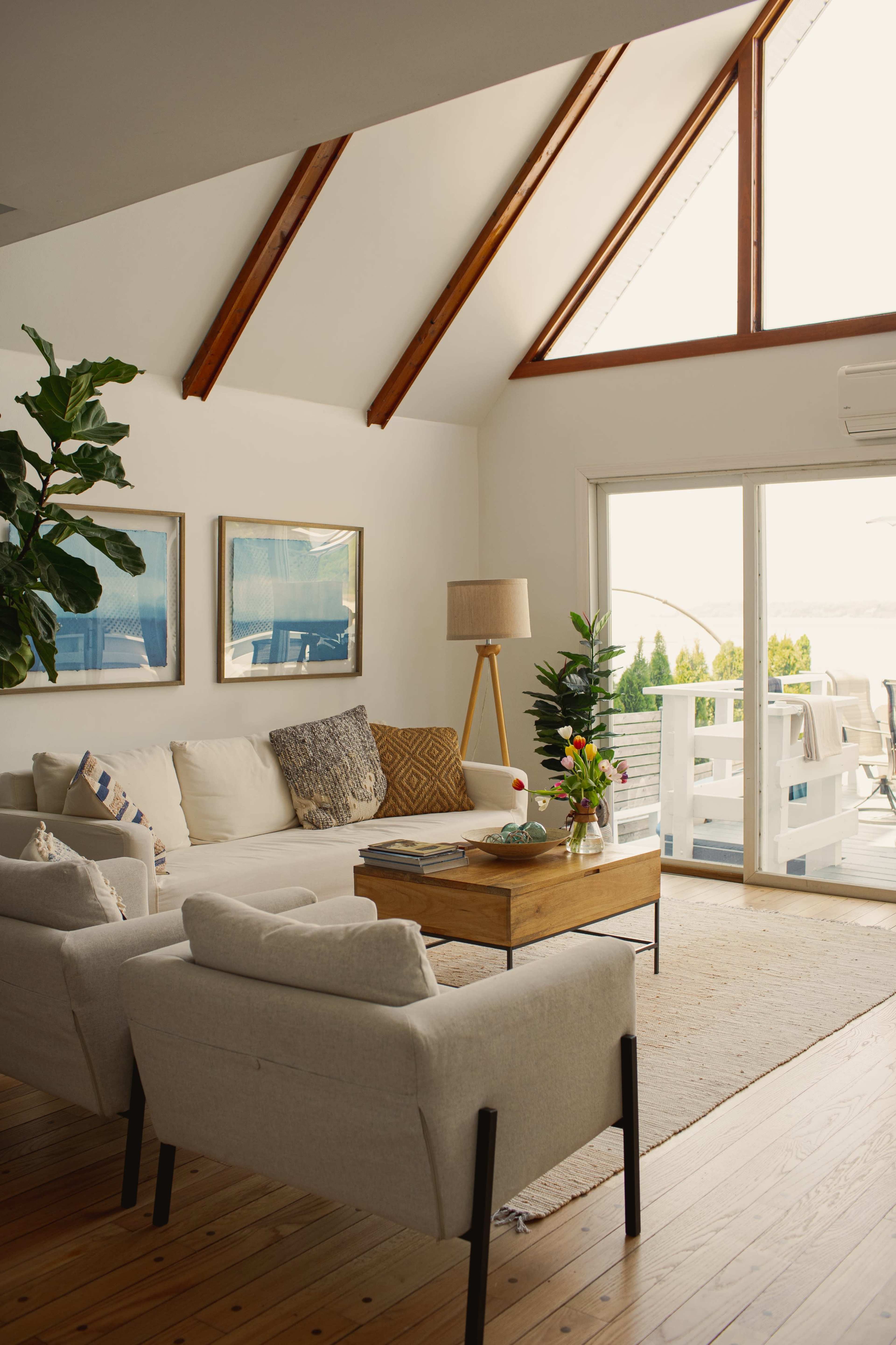 A modern living room with a high ceiling, large windows, and comfortable seating arrangements around a wooden coffee table.