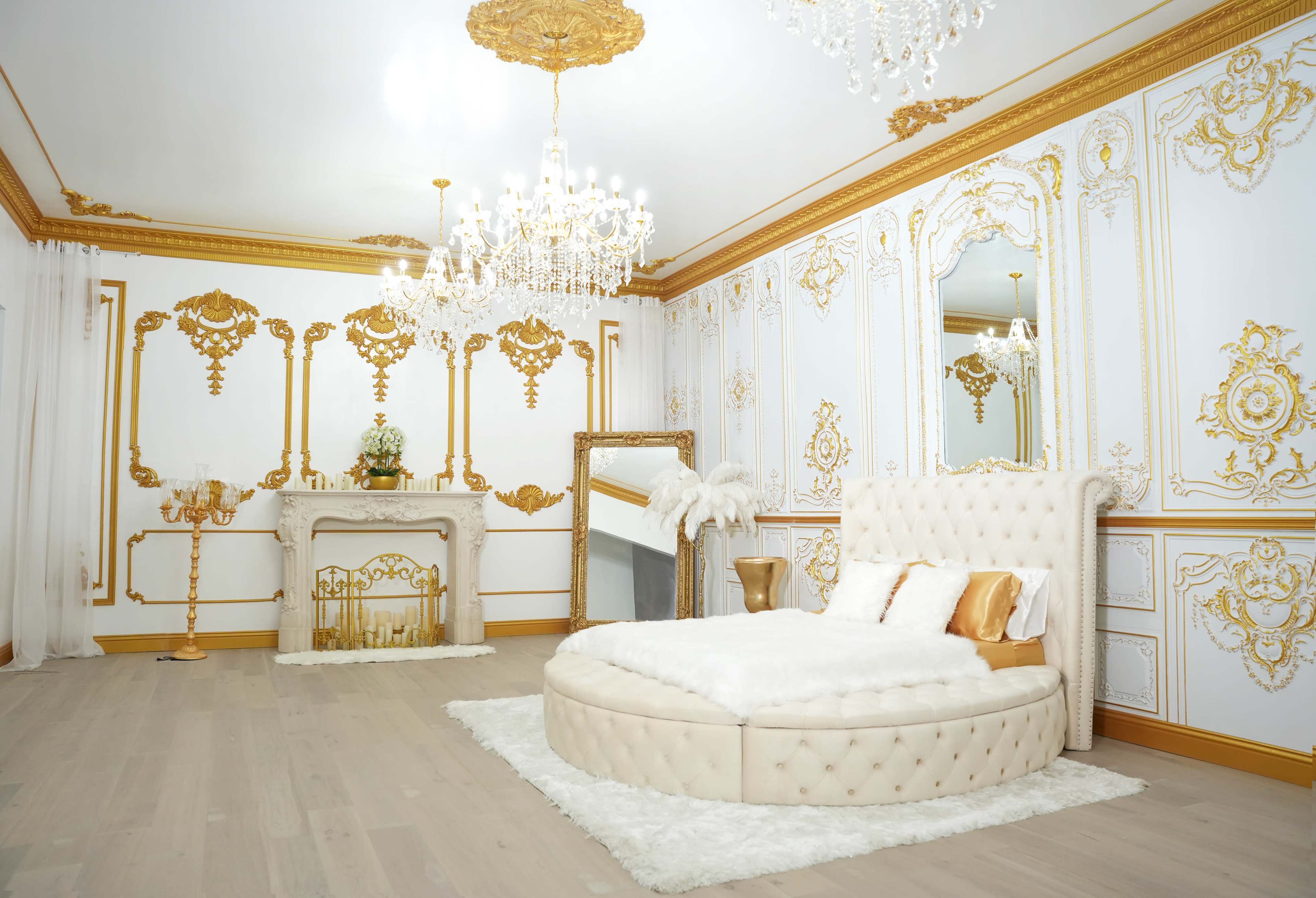 An elegantly decorated bedroom featuring a circular upholstered bed, a decorative fireplace, and ornate golden wall accents.