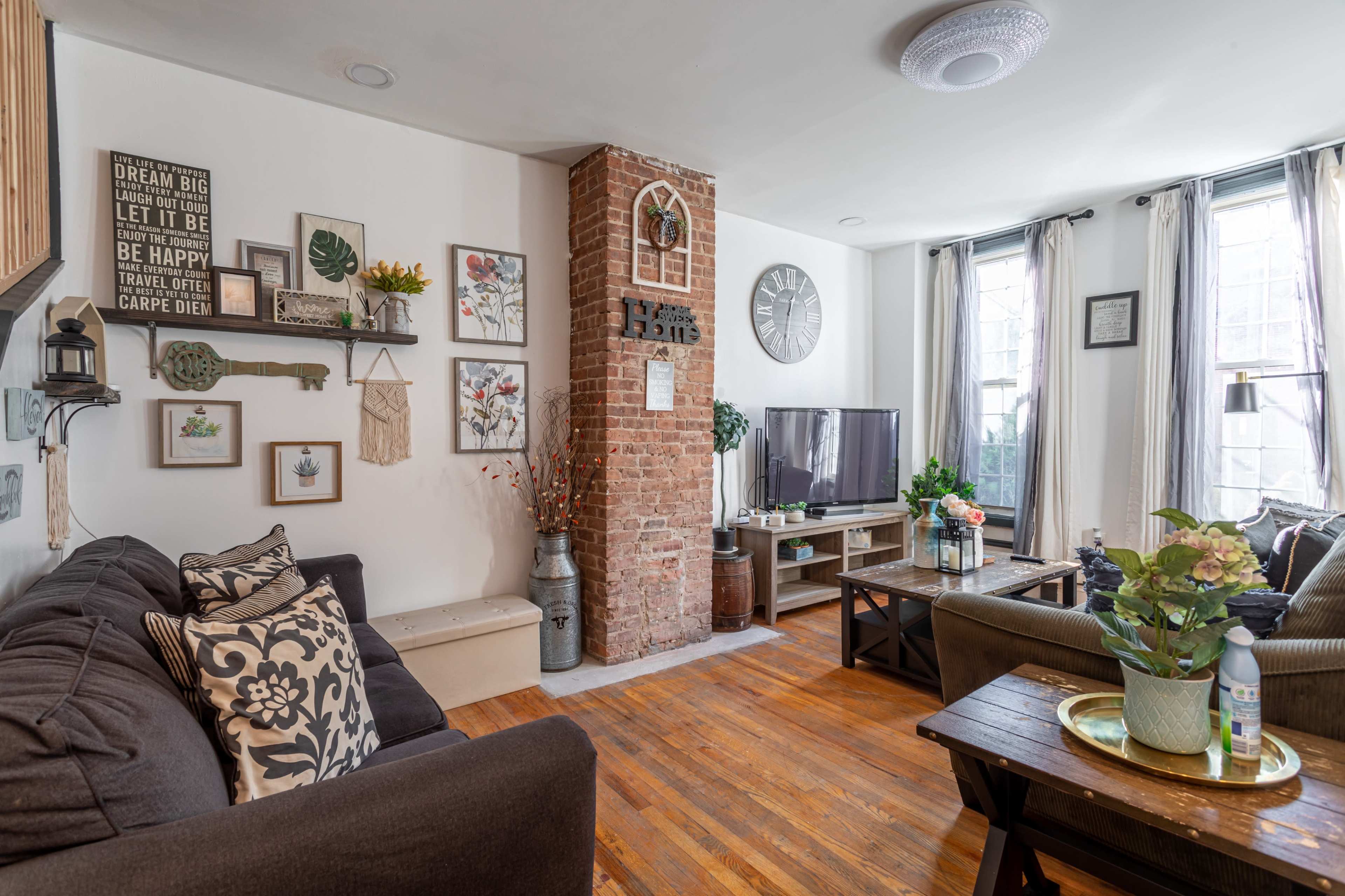 A cozy living room with a brick accent wall, a television, wooden furniture, and decorative plants.