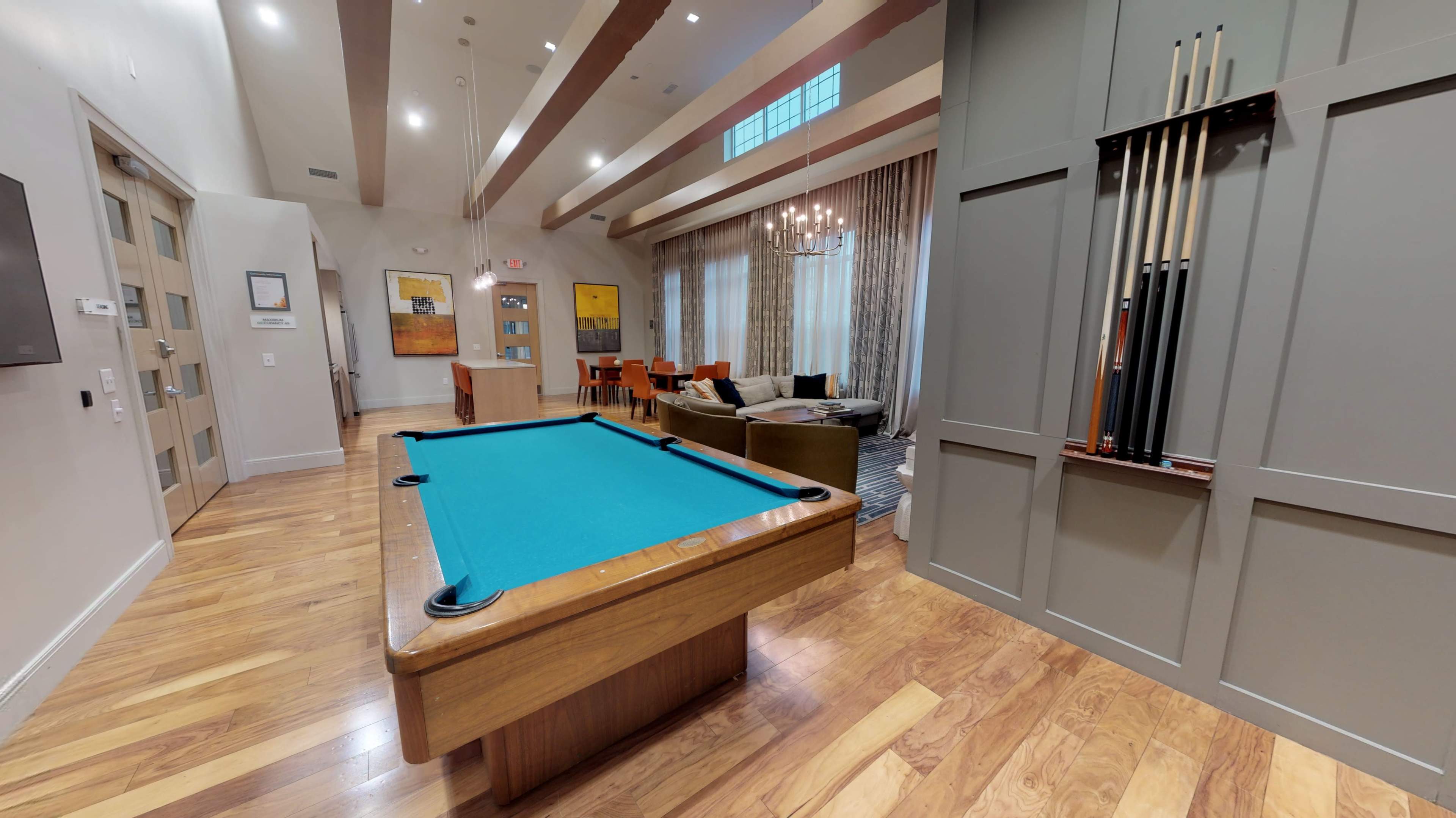 A recreational room featuring a slate pool table with a turquoise felt surface, wooden flooring, and a seating area in the background.