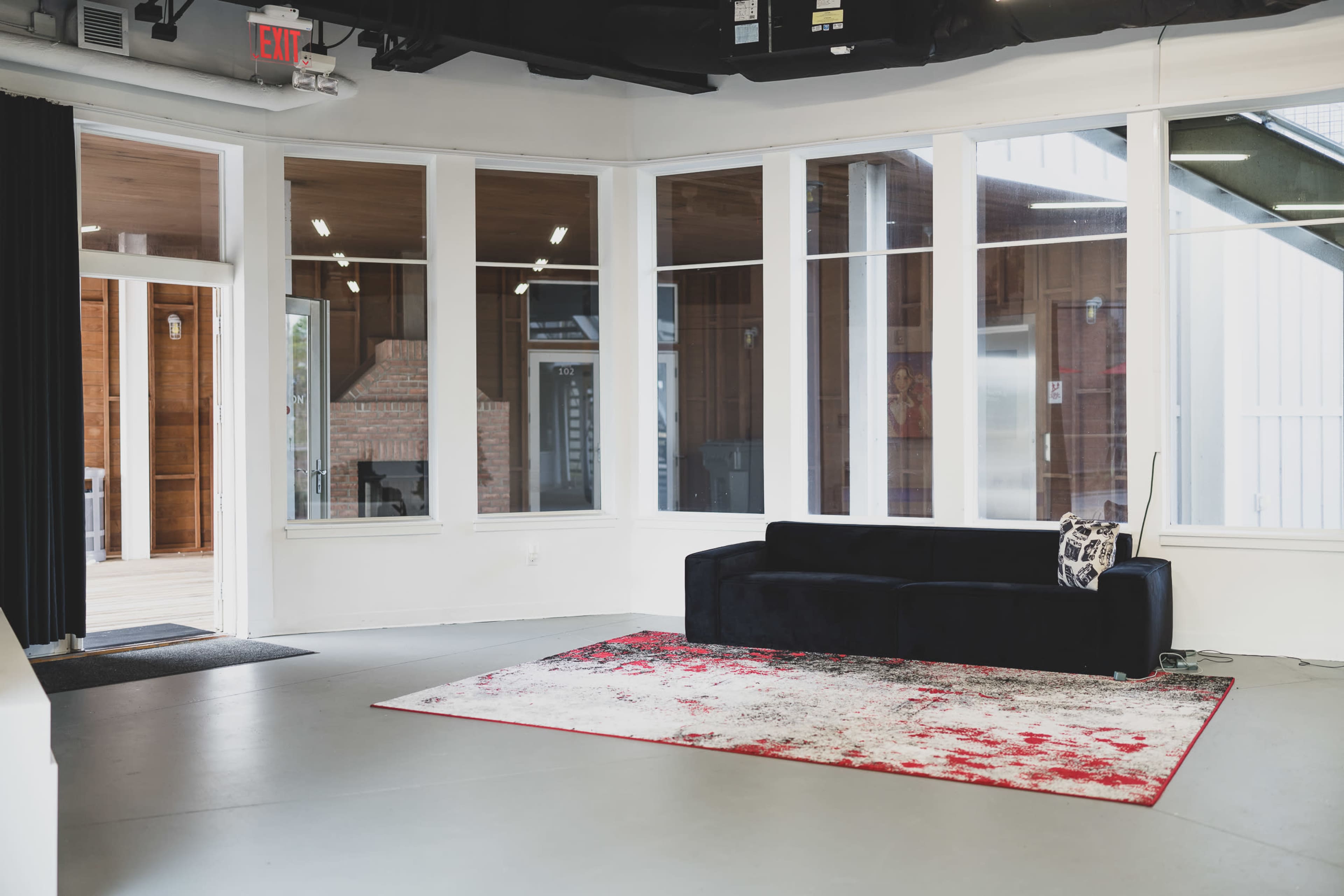 A modern interior space features a black sofa on a patterned rug, surrounded by large windows.