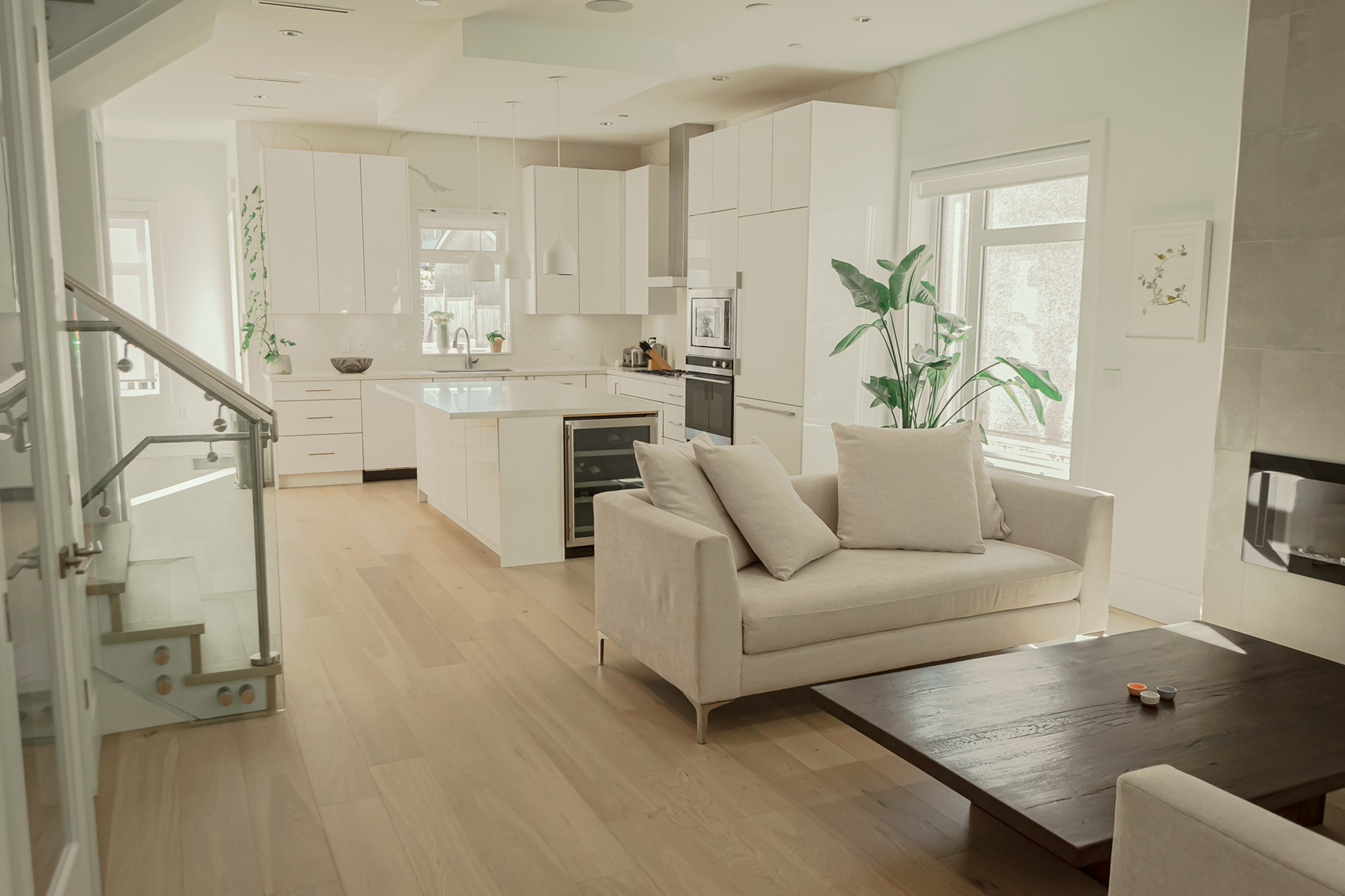 A modern kitchen and living area feature white cabinetry, a large island, and a comfortable sofa facing a coffee table.