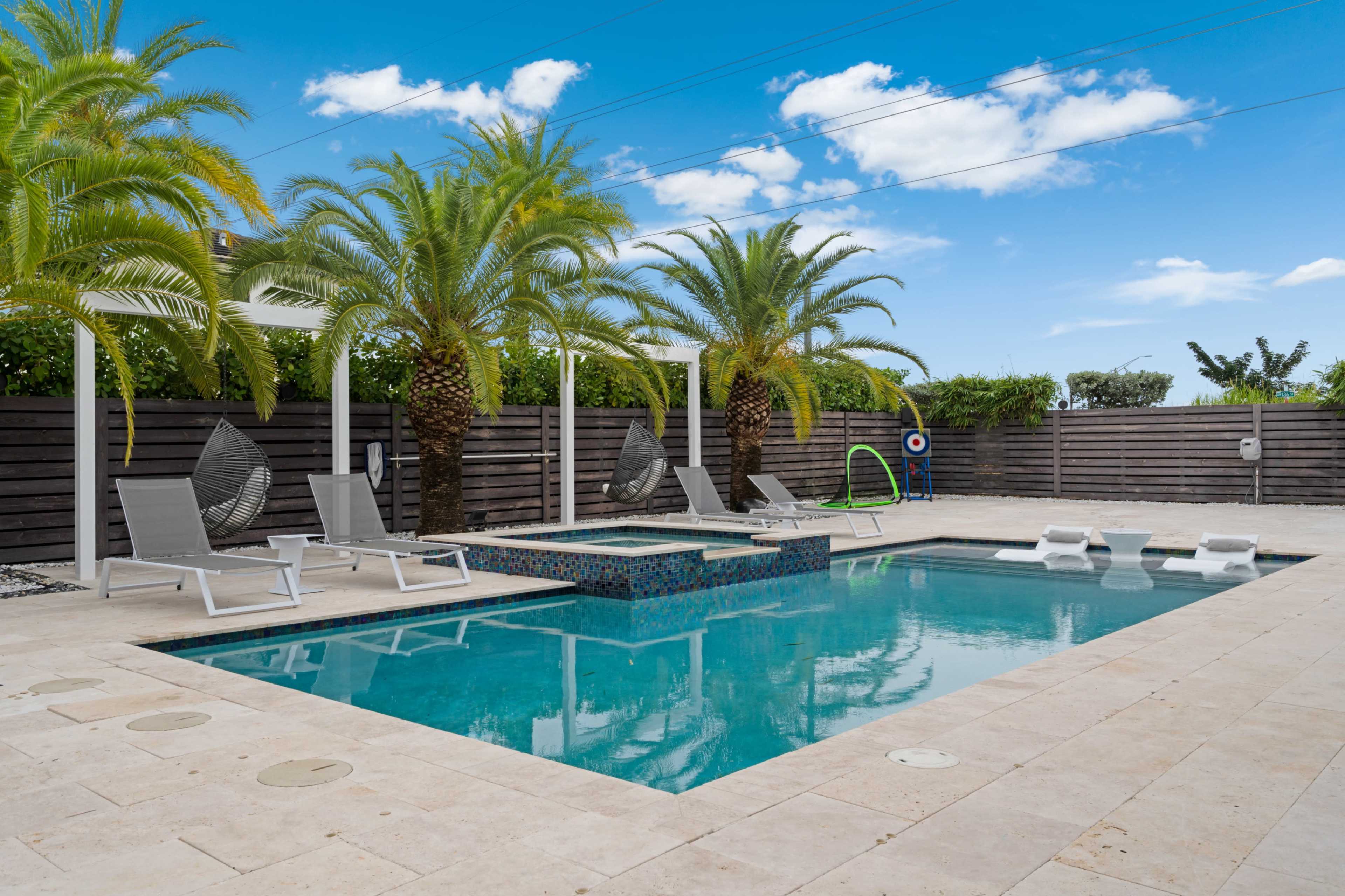 A swimming pool surrounded by palm trees, lounge chairs, and a spa area, with a clear blue sky above.