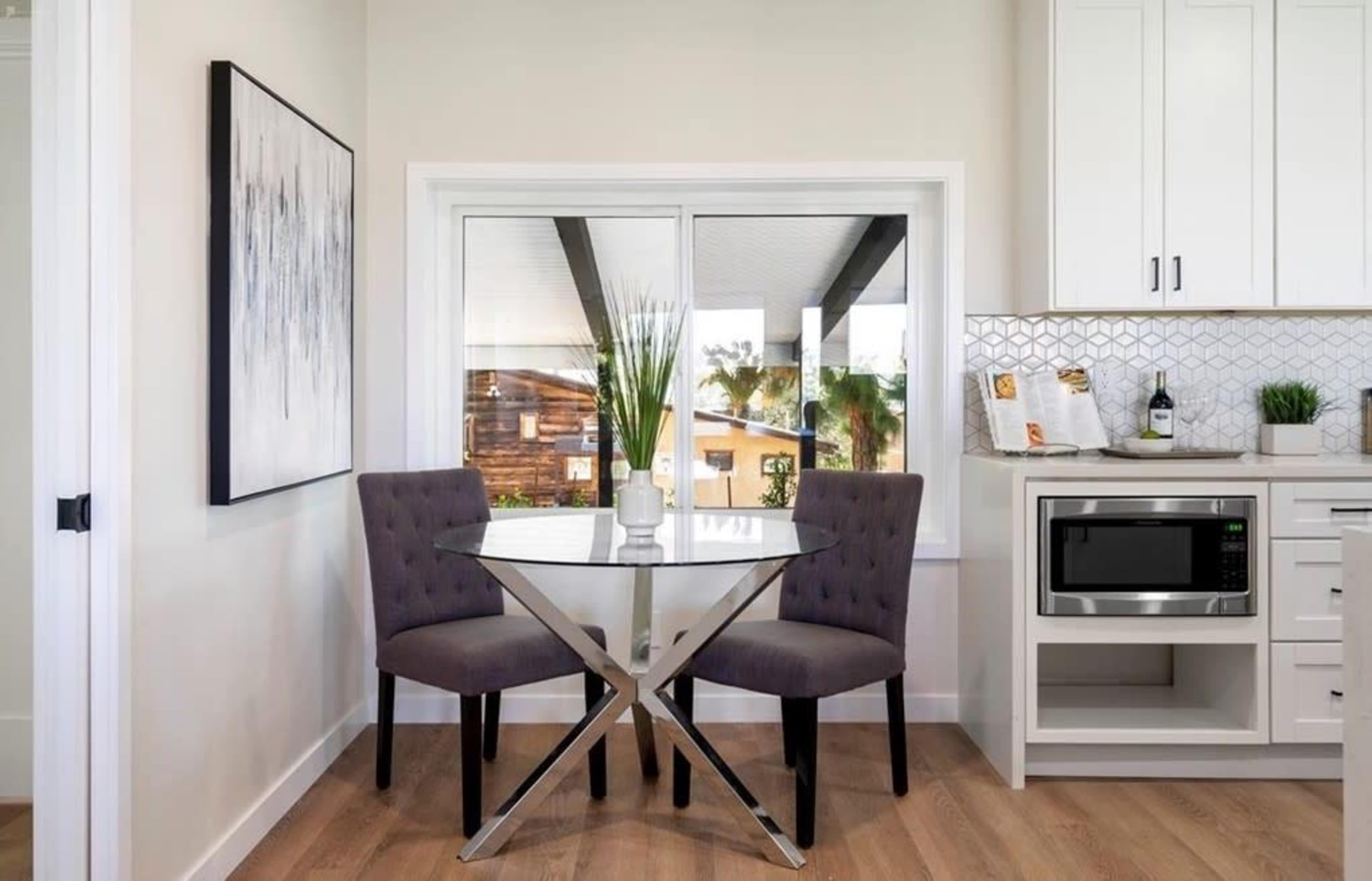 A small dining area features a round glass table with two upholstered chairs, positioned near a window overlooking a patio.