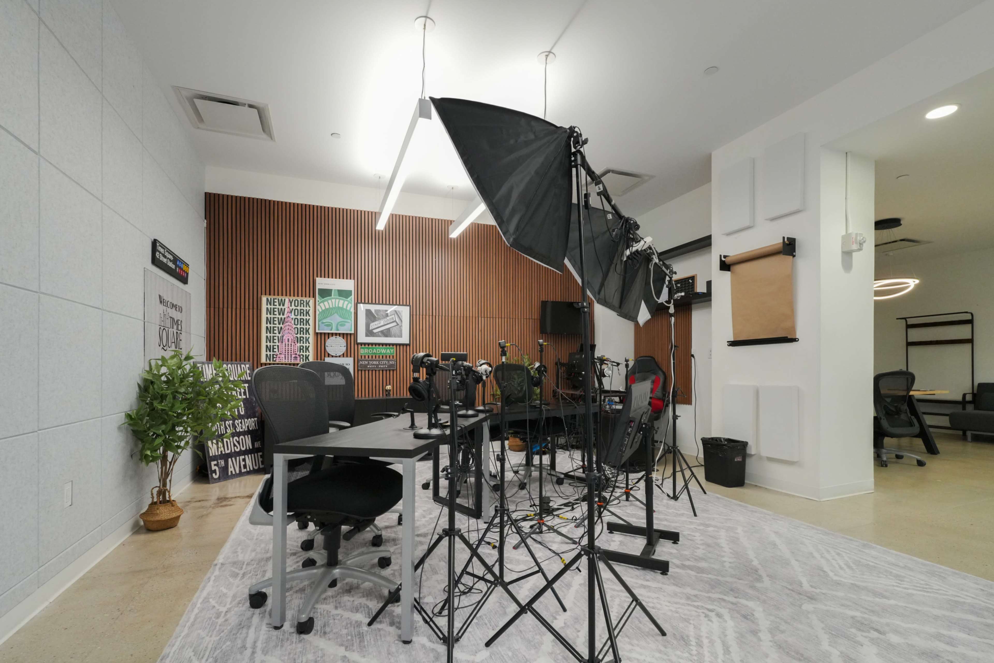 The image shows a modern workspace setup with studio equipment, including lights and cameras, arranged around a table and chairs in a well-lit environment.