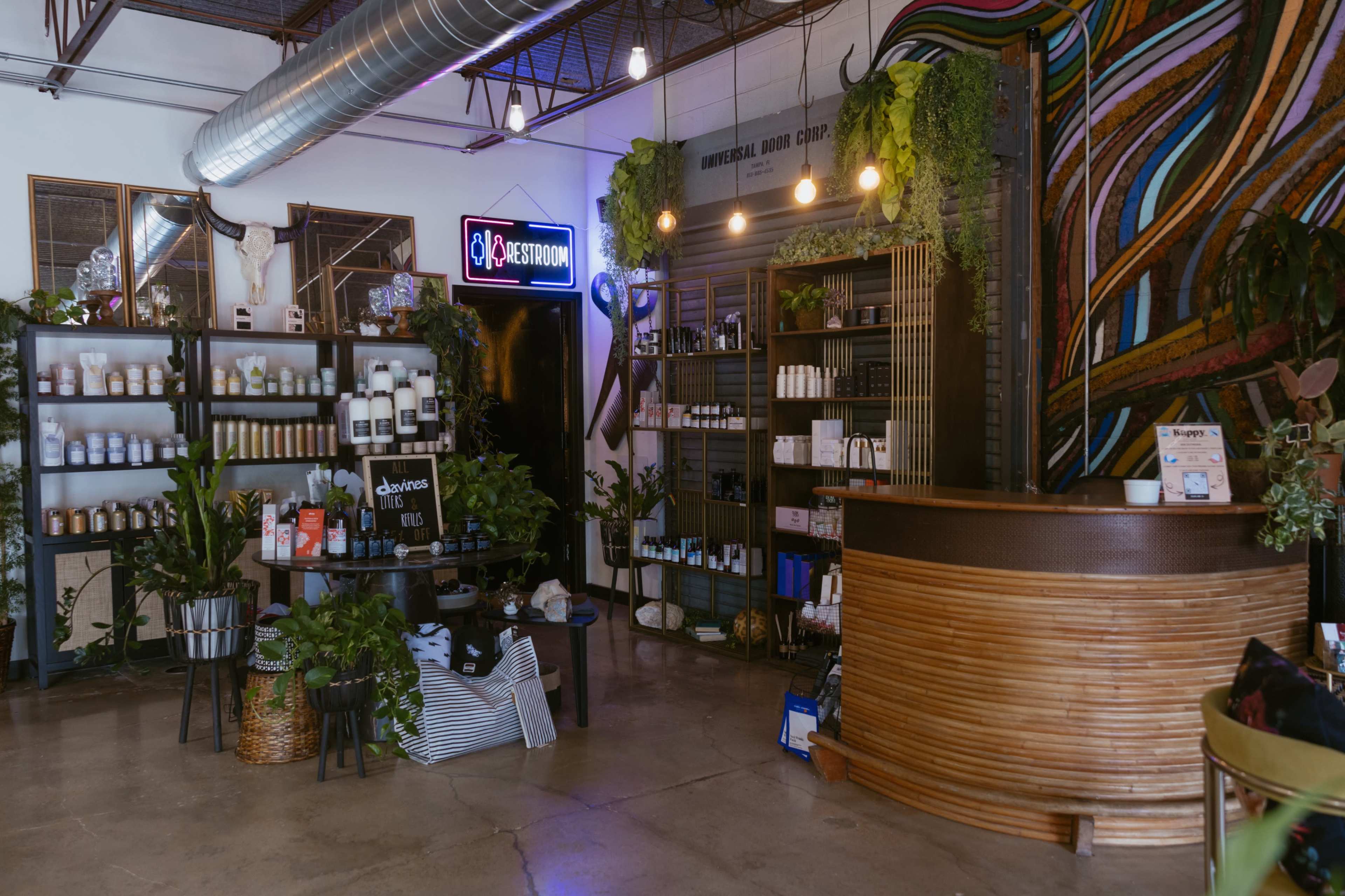 The image shows a modern retail space with wooden displays, shelves filled with various products, and a colorful mural on the wall.