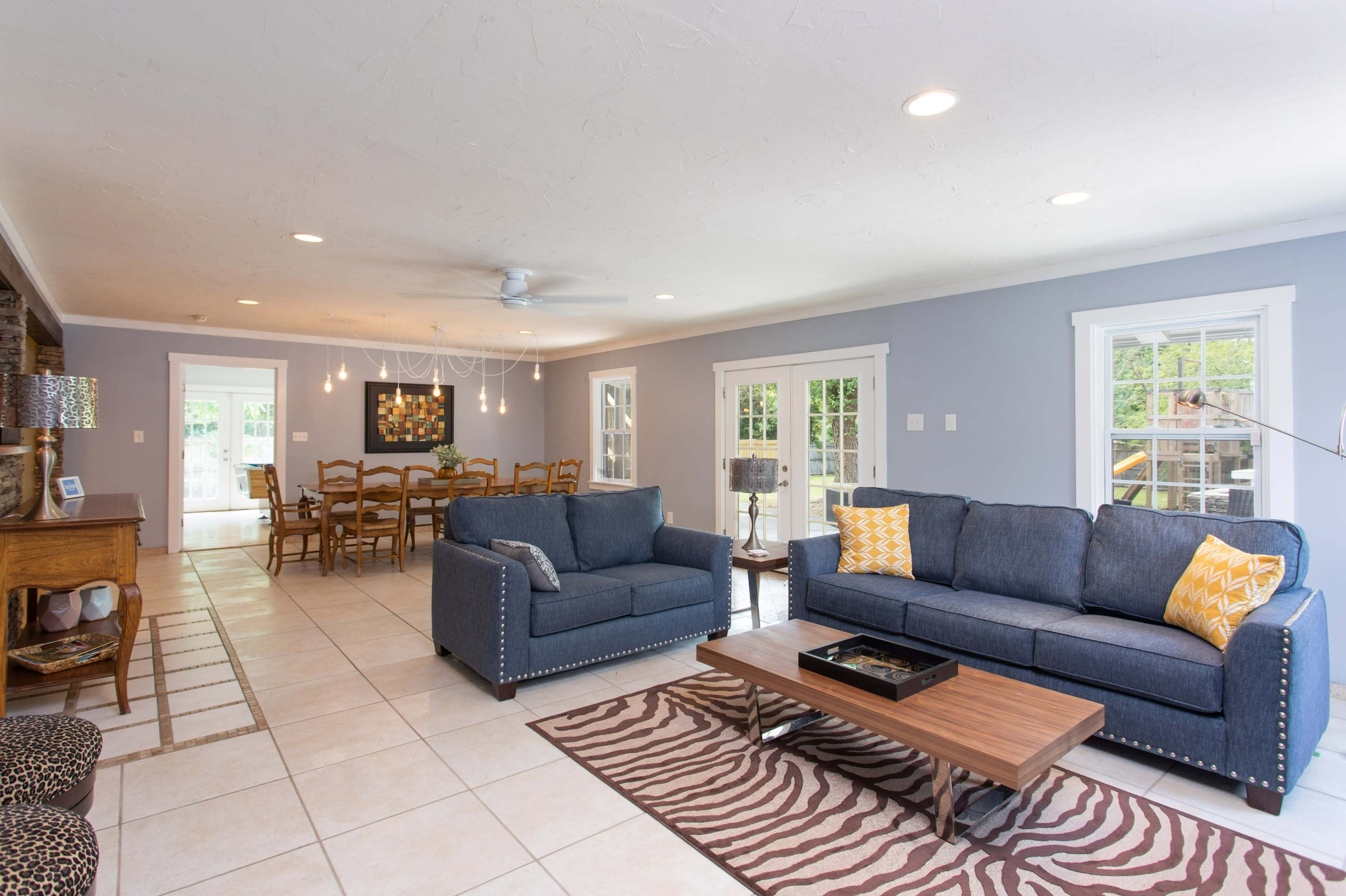 The spacious living area features two dark sofas, a wooden coffee table, and a view of a dining area through large windows.