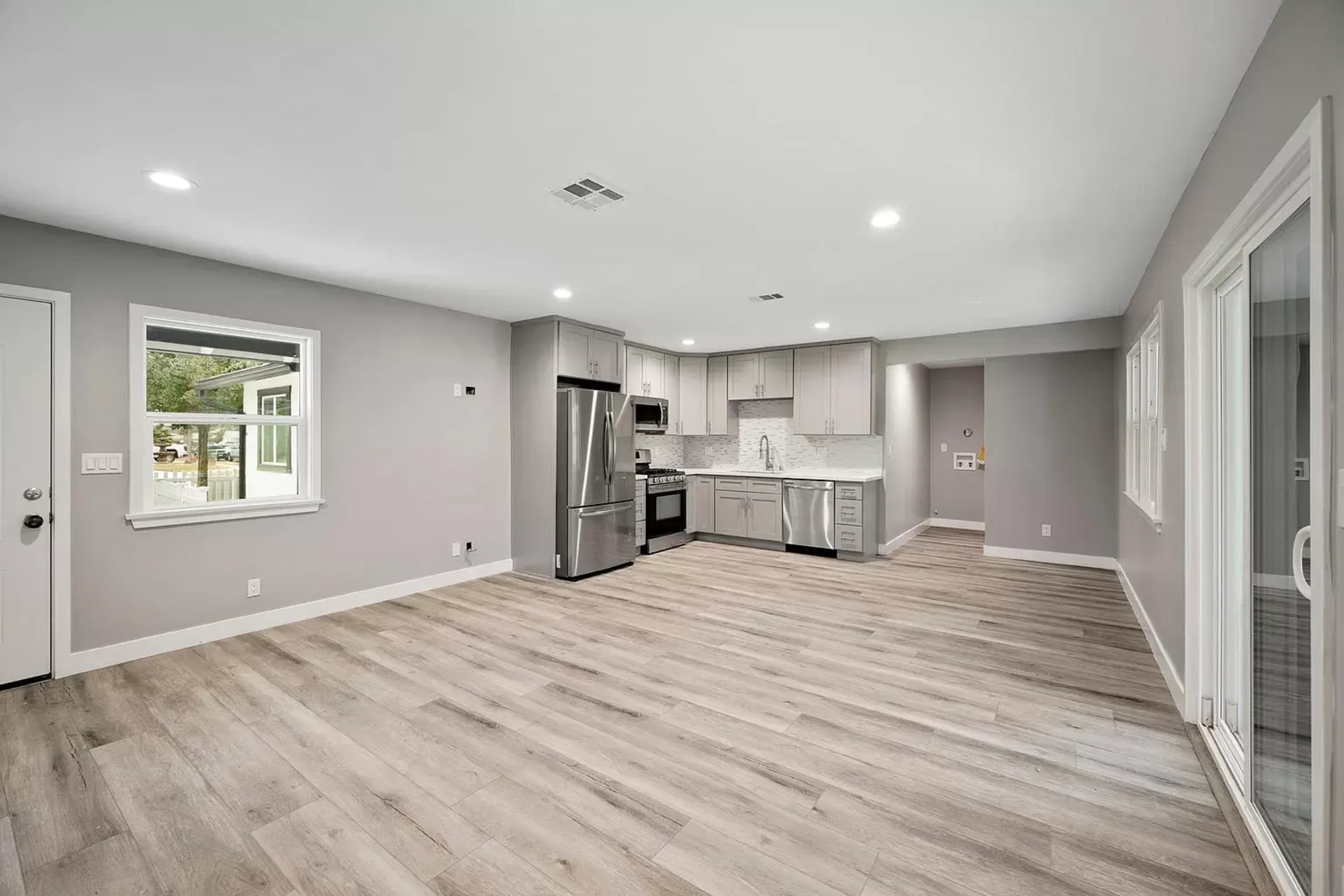 A modern, open-concept kitchen and living area with light wood flooring, gray walls, and stainless steel appliances.