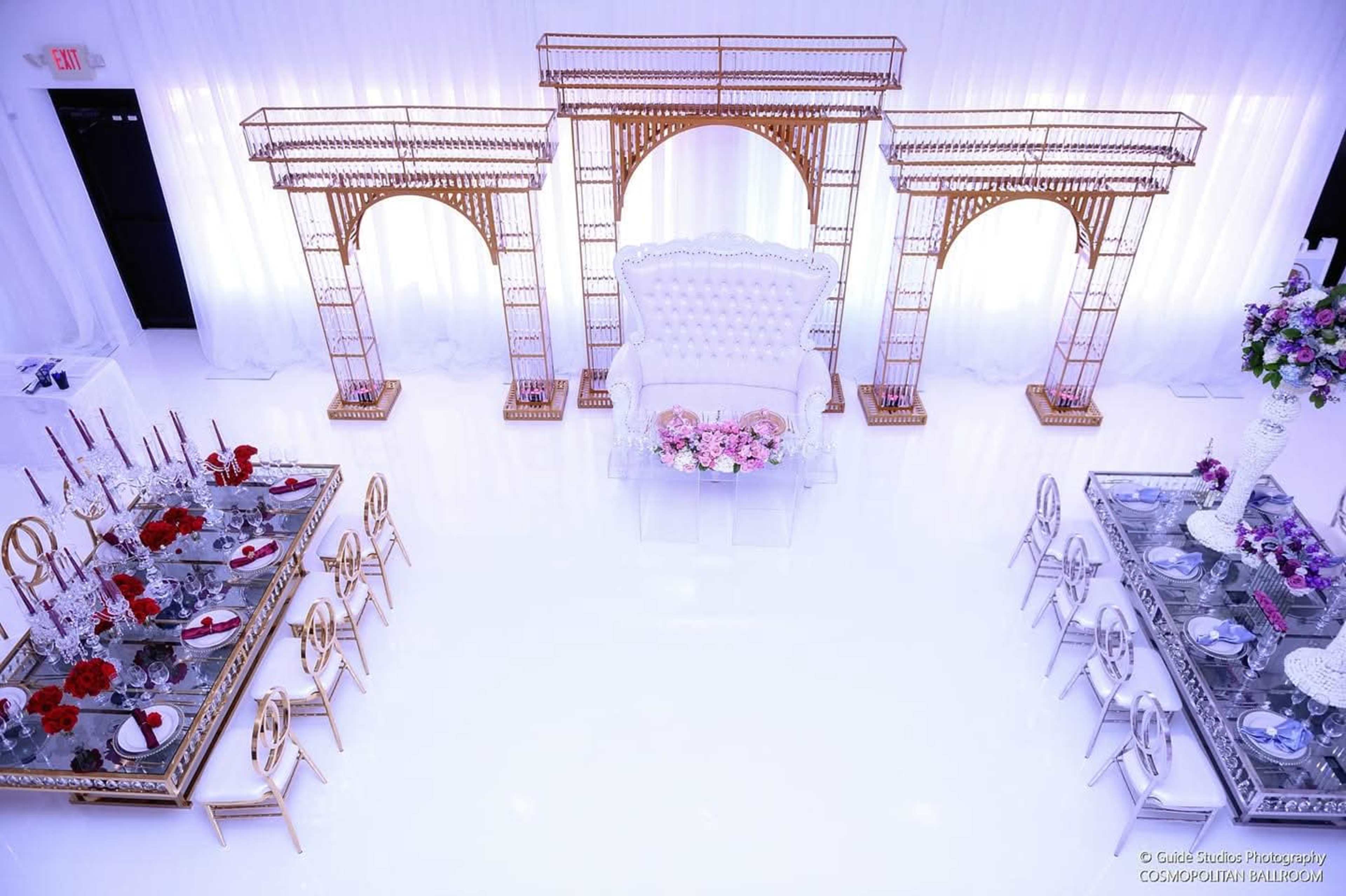 The image depicts a lavish event space featuring elegant tables set with fine dining arrangements and a grand seating area with decorative arches in the background.