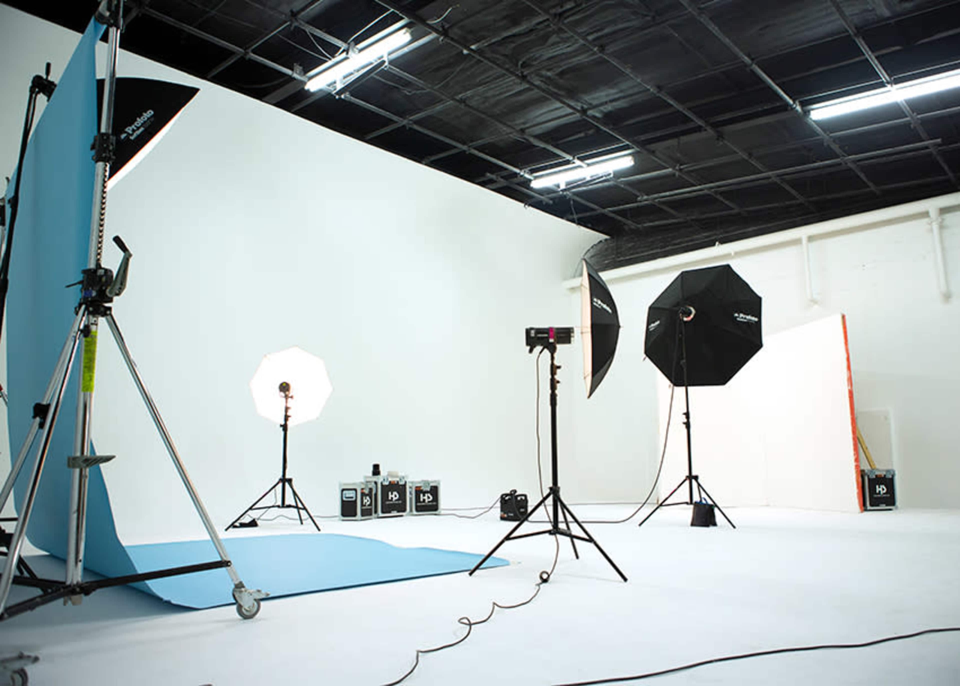 A photography studio with a white backdrop, lighting equipment, and a blue fabric on the floor.