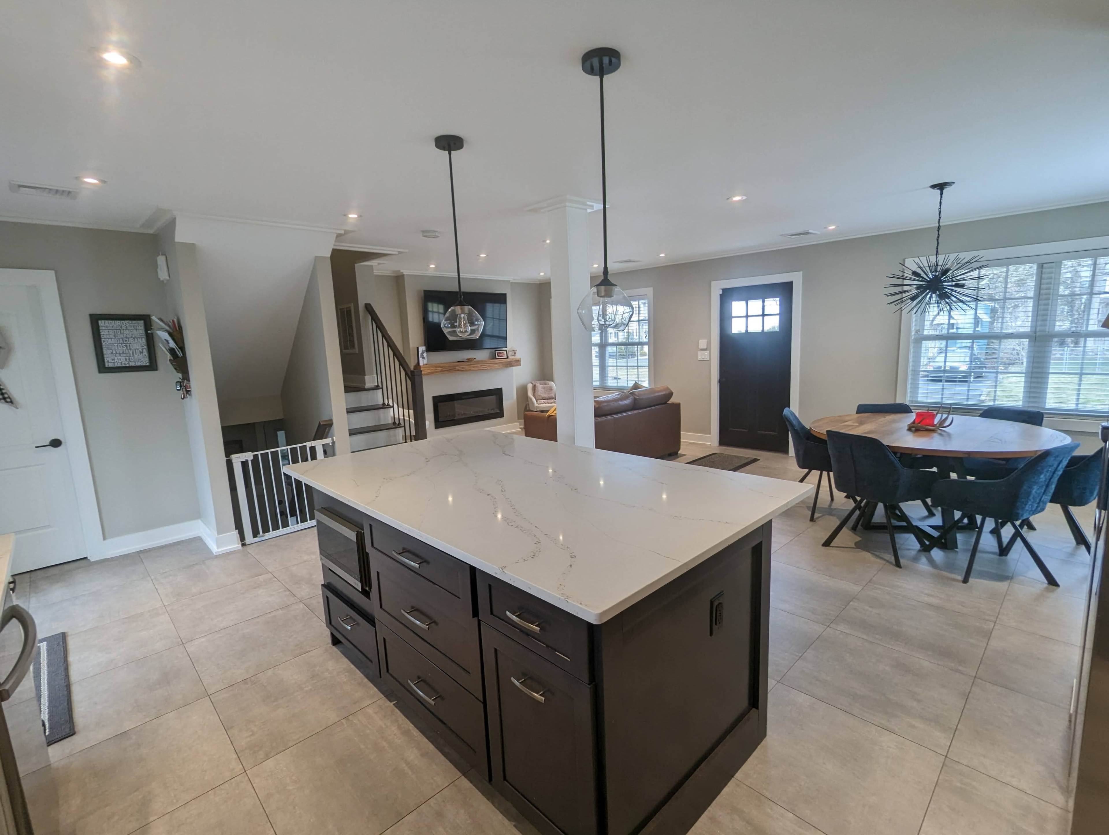 A modern kitchen features a central island, a dining area with a round table, and a staircase leading to a living space.