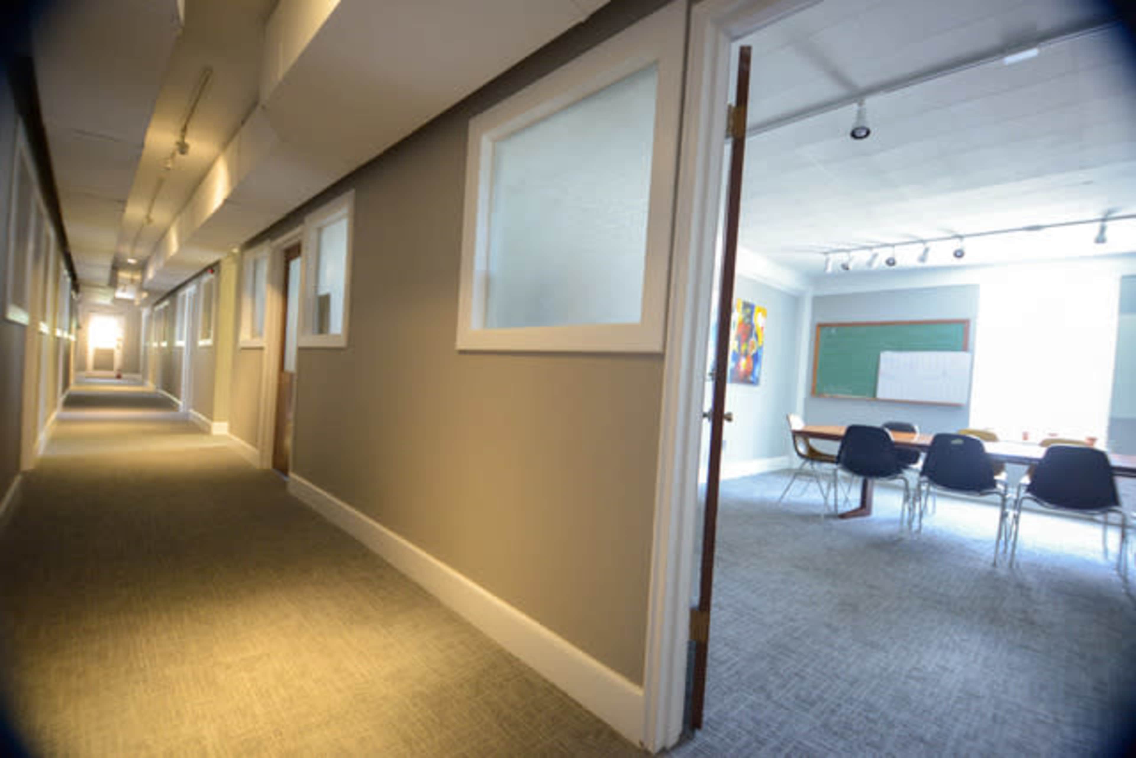 A hall lined with doors leading to individual offices, with a conference room visible at the end of the corridor.