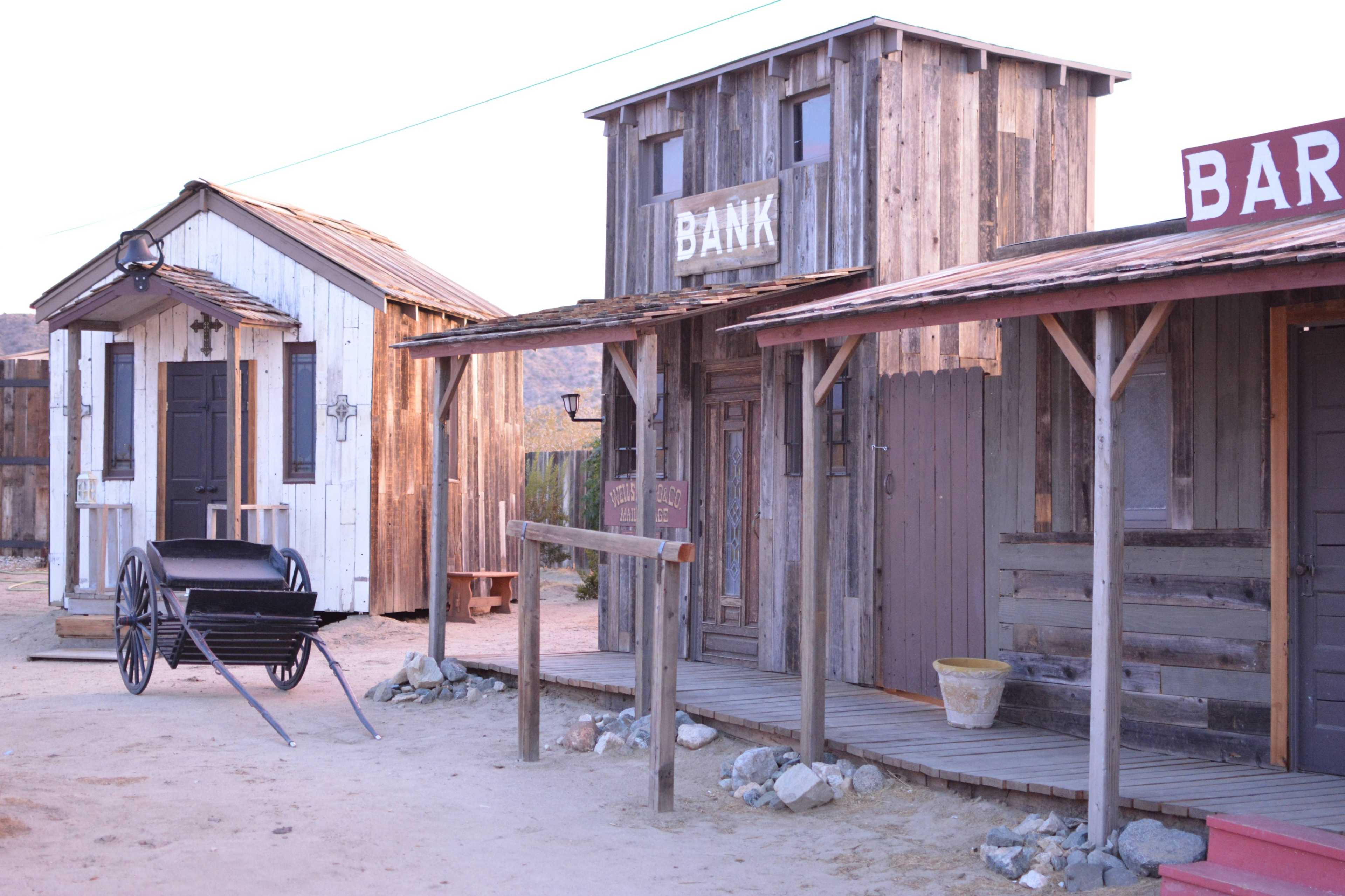 The scene shows a western-style town with wooden structures labeled "BANK" and "BAR," and a black cart positioned on the dirt path between the buildings.