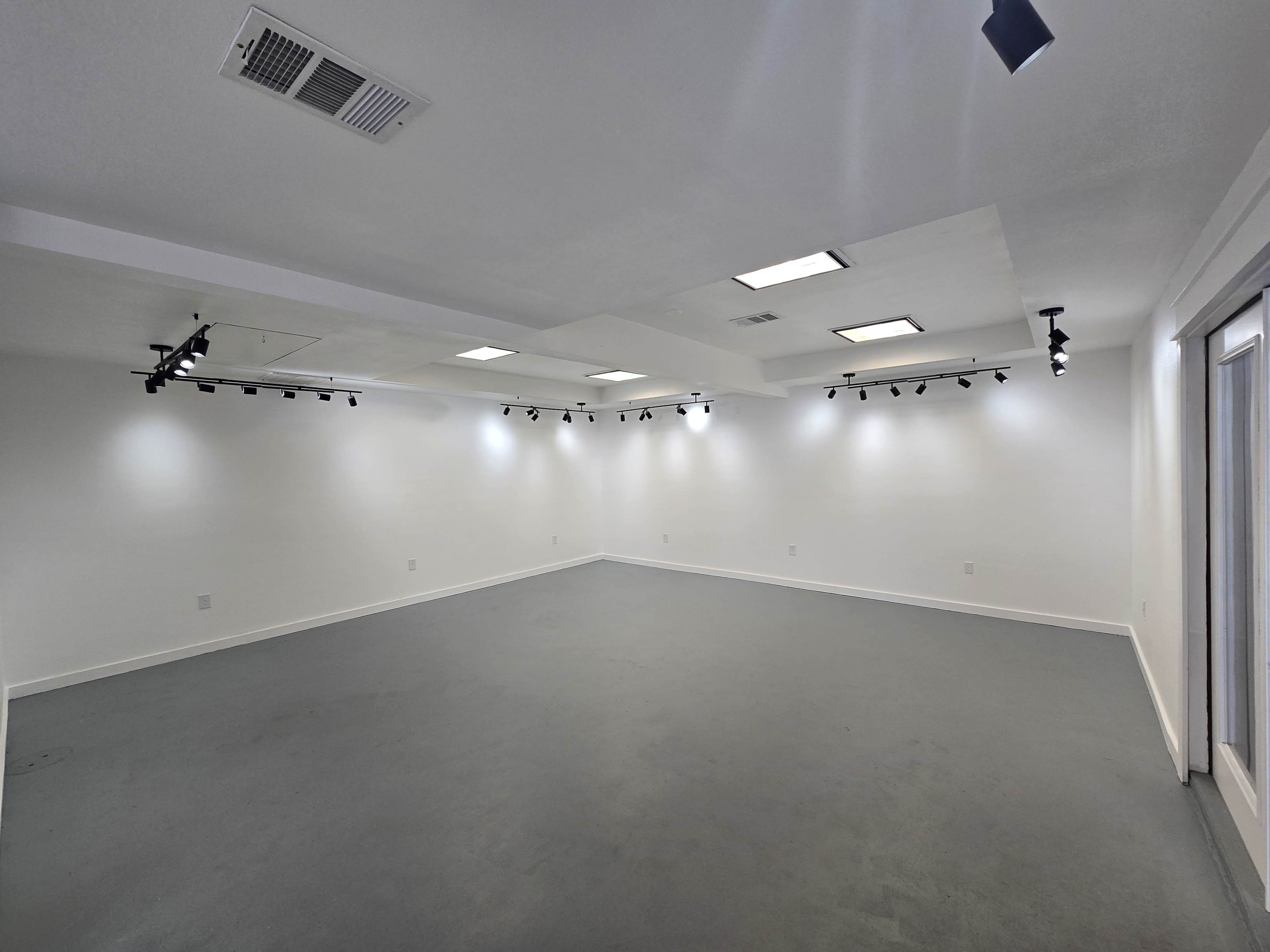 The image shows a spacious, empty room with gray flooring and overhead track lighting.