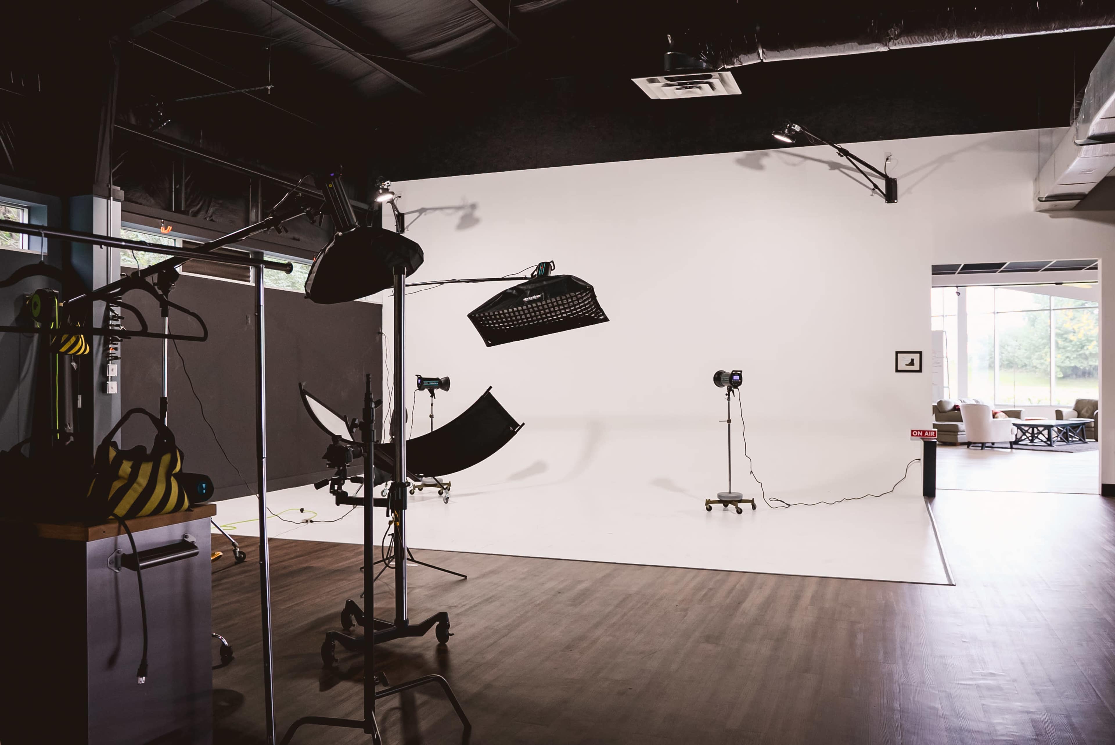 A photography studio features a backdrop setup with lighting equipment and a large white wall.
