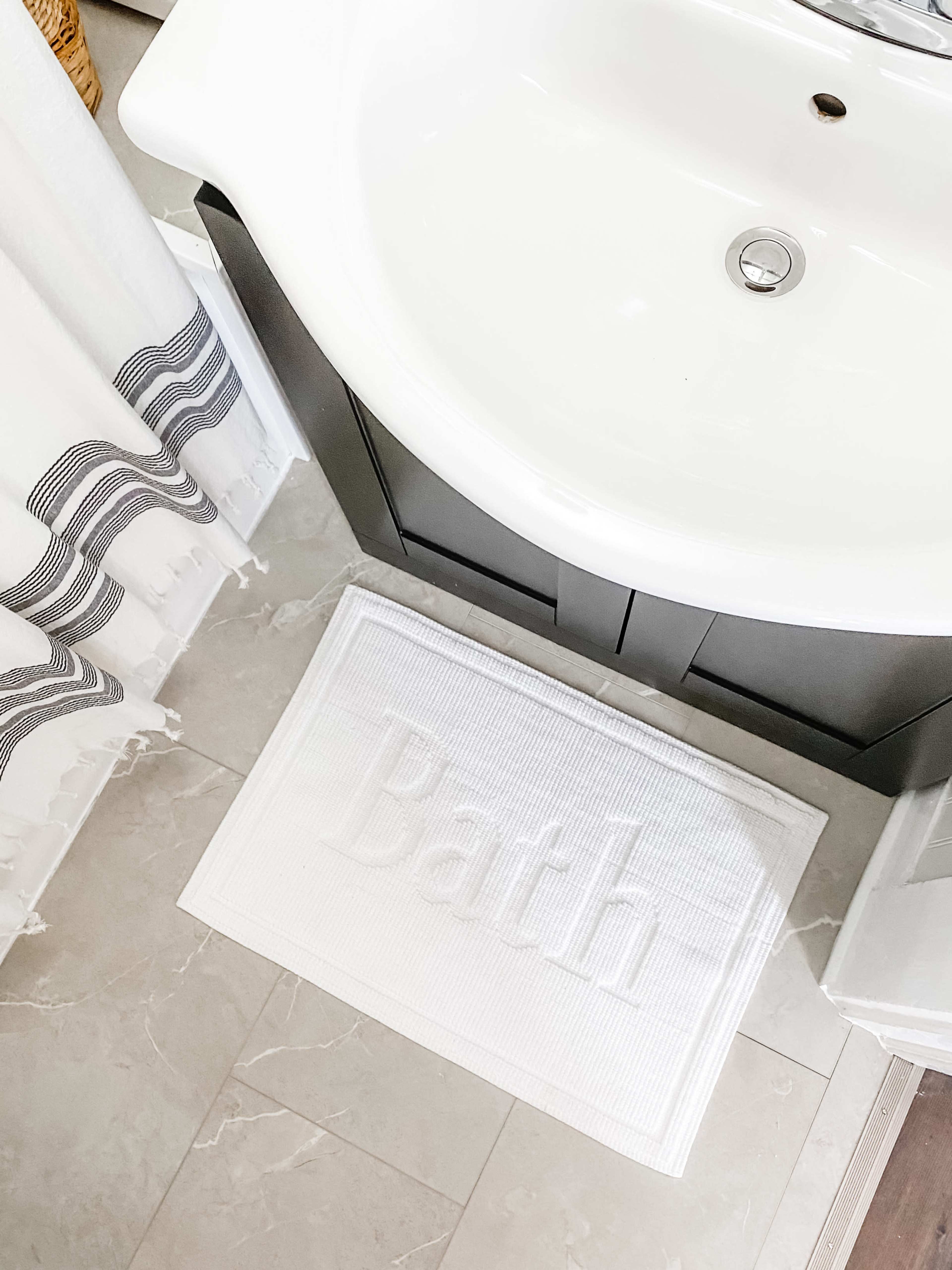A white bath mat with the word "Bath" is placed in front of a sink in a bathroom.