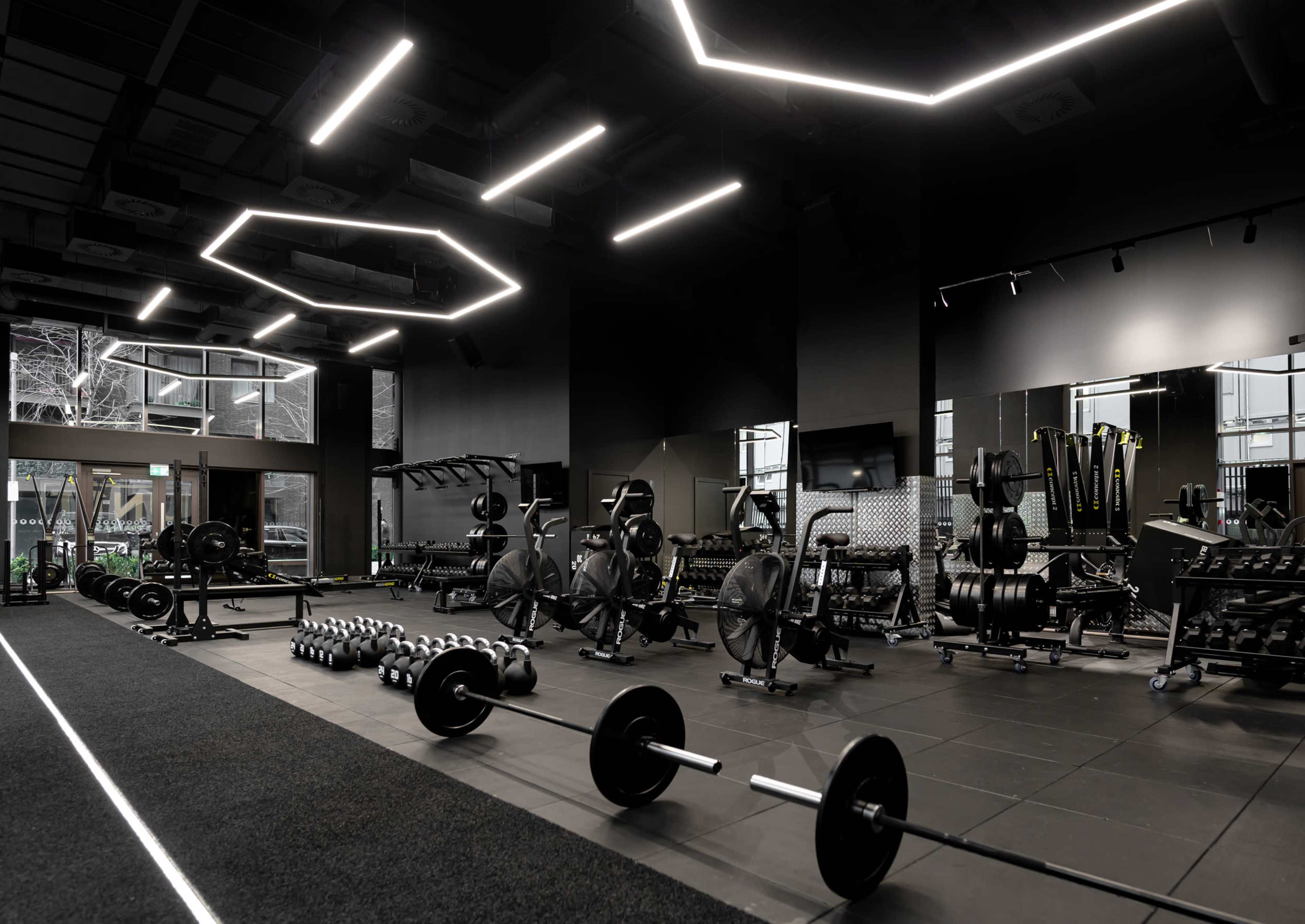 The gym features black walls, large mirrors, and various weightlifting equipment arranged neatly along the space.
