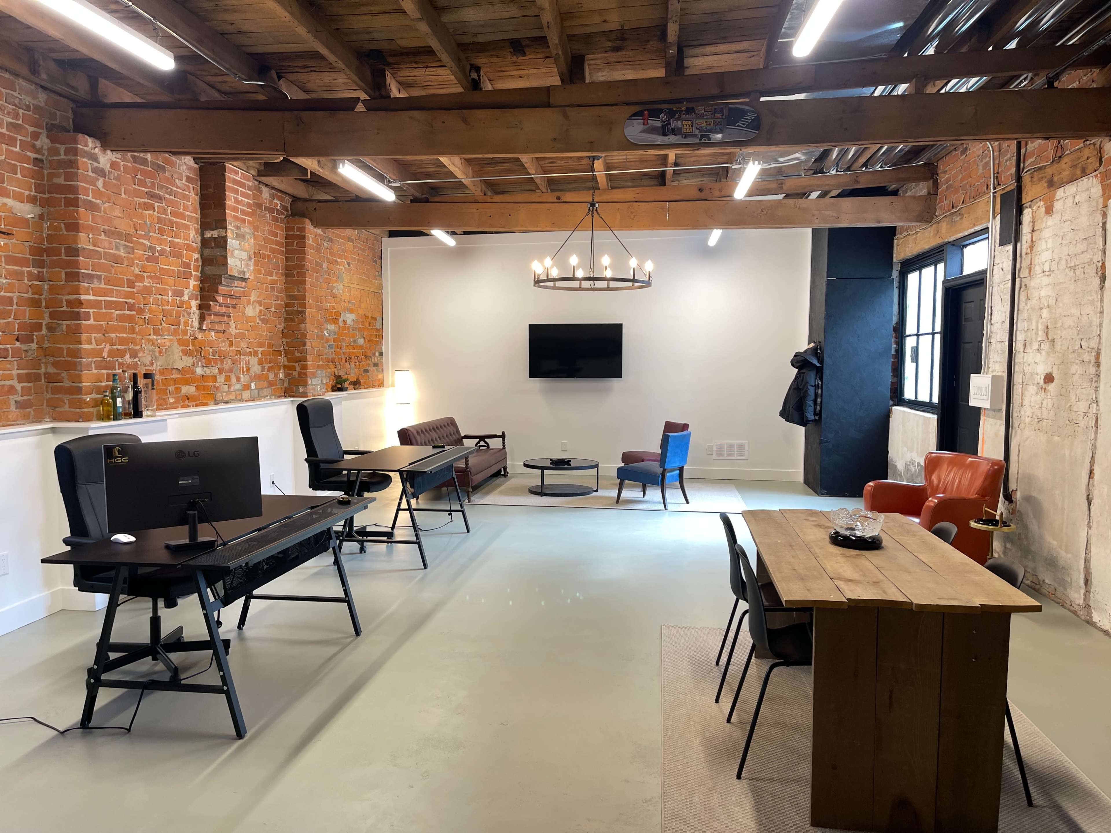 A modern office space featuring rustic brick walls, a wooden ceiling, various workstations, and a seating area with multiple chairs and a table.