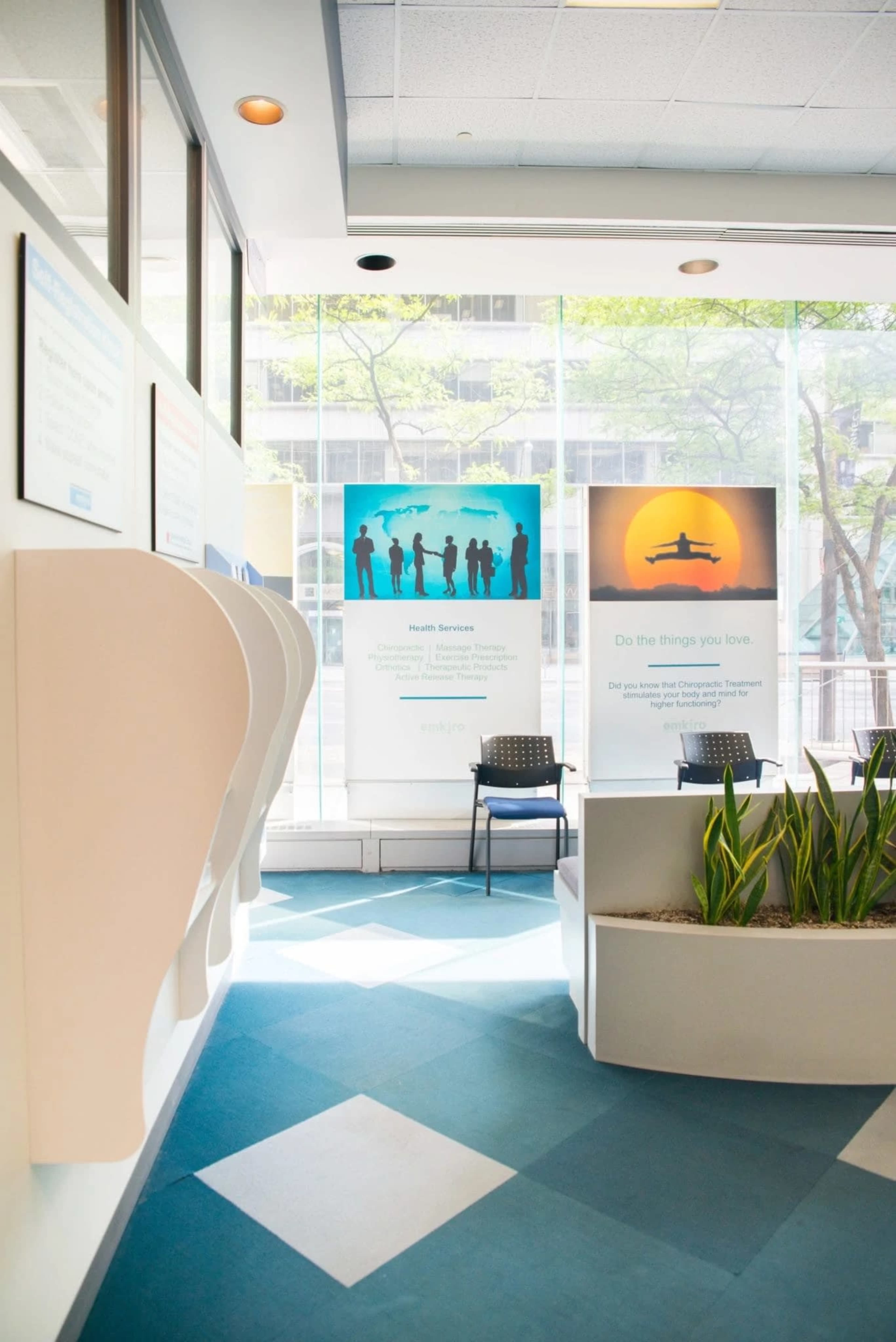 A bright, modern waiting area with informational panels on the walls, a chair, and a planter with greenery.