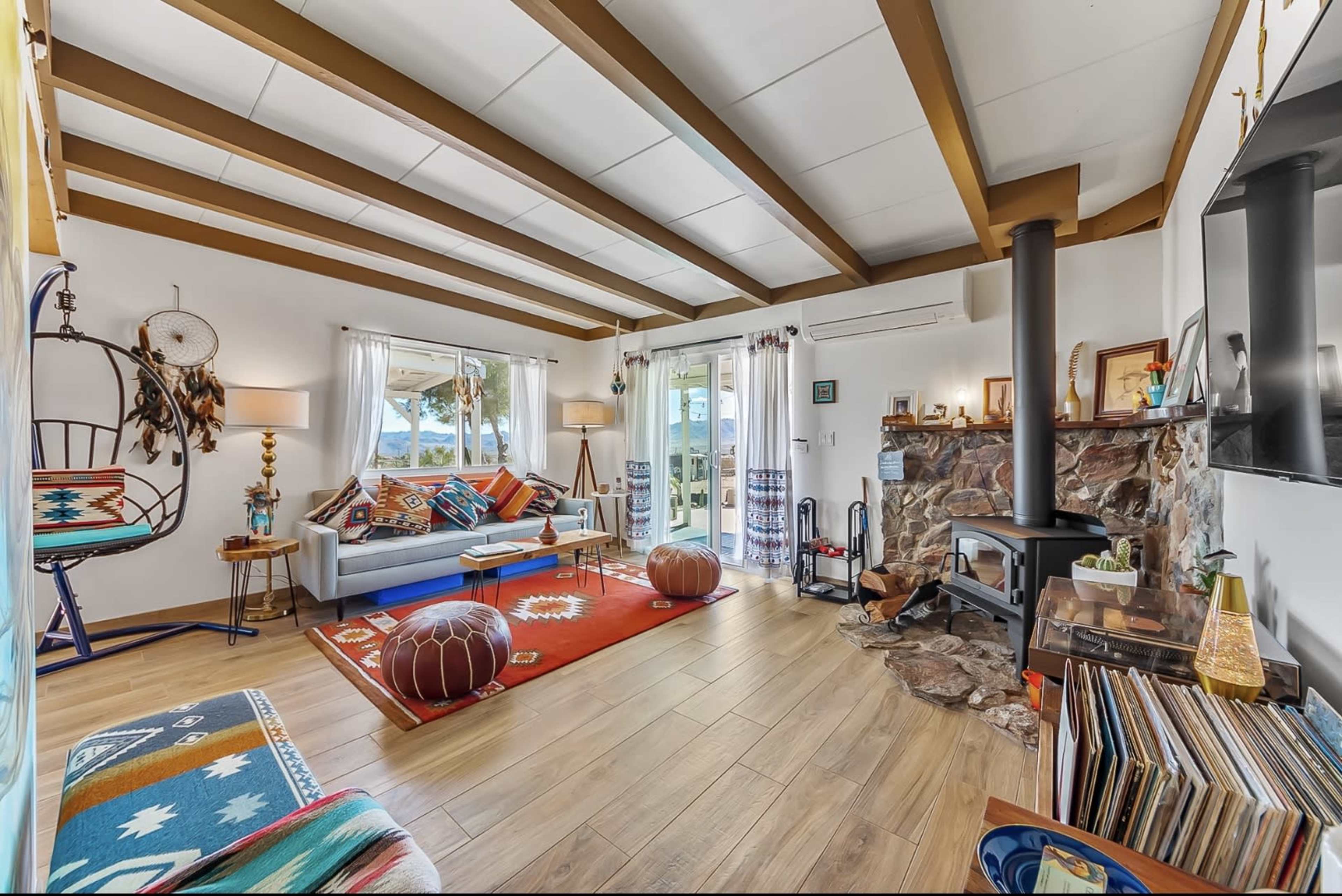 The living room features a combination of rustic and modern design elements, including a fireplace, window seating, and colorful textiles.