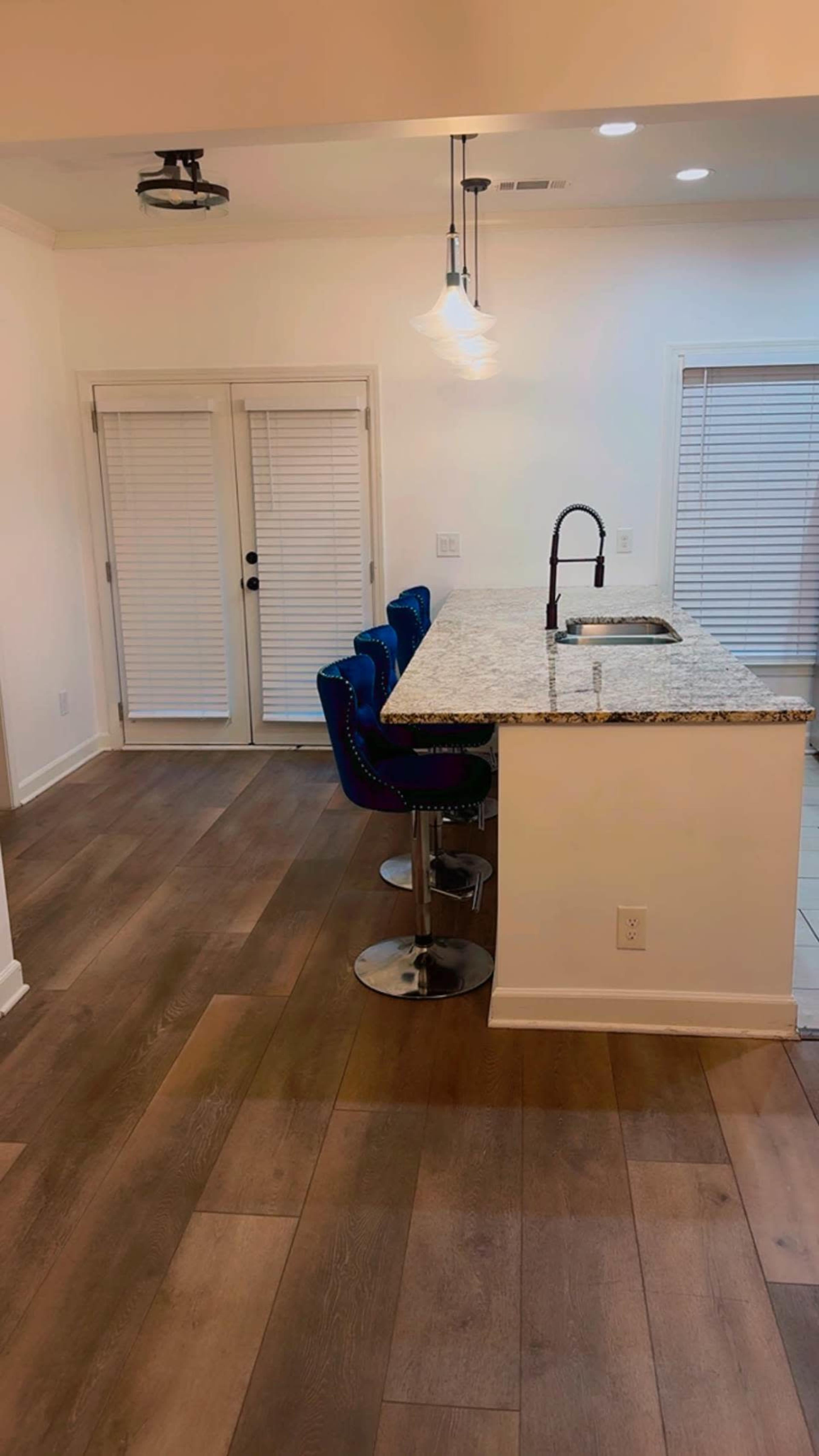 The image shows a modern kitchen with a granite countertop and four blue bar stools facing a wall of white sliding doors.