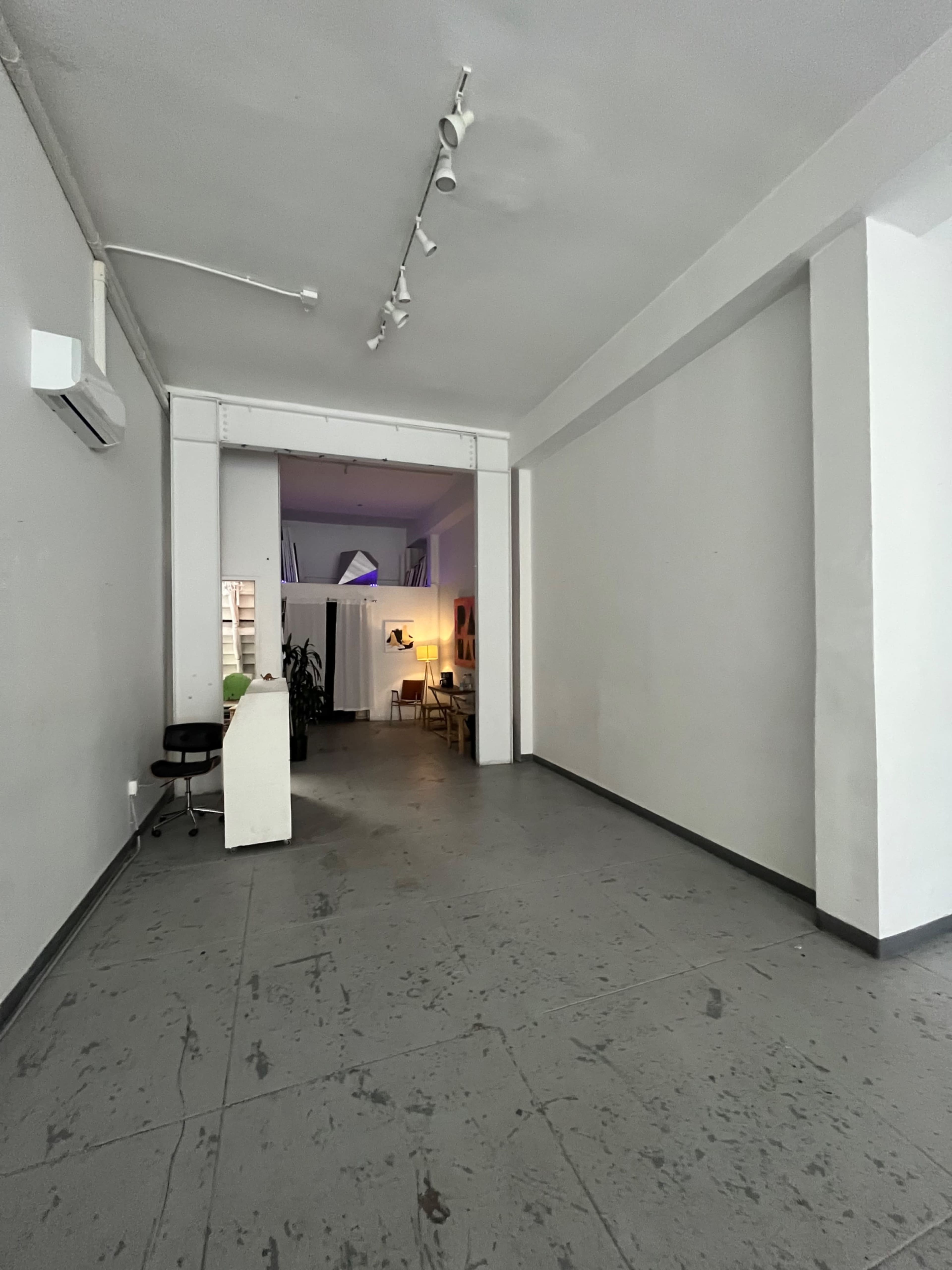 A spacious, empty room with concrete flooring and white walls, featuring a doorway leading to a brightly lit area in the background.