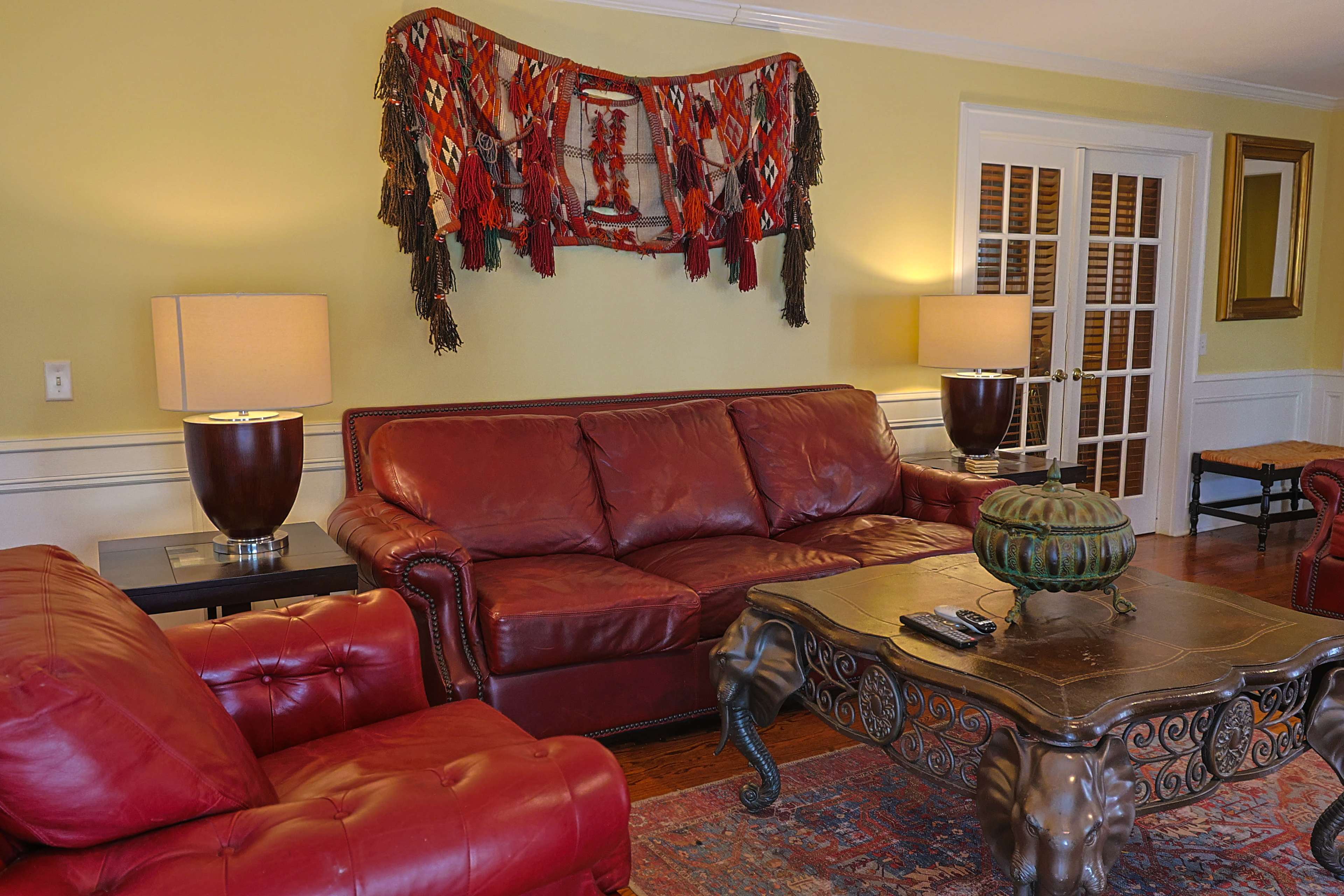The image features a living room with a red leather sofa and armchair, a decorative wall hanging, and a coffee table with a phone on it.