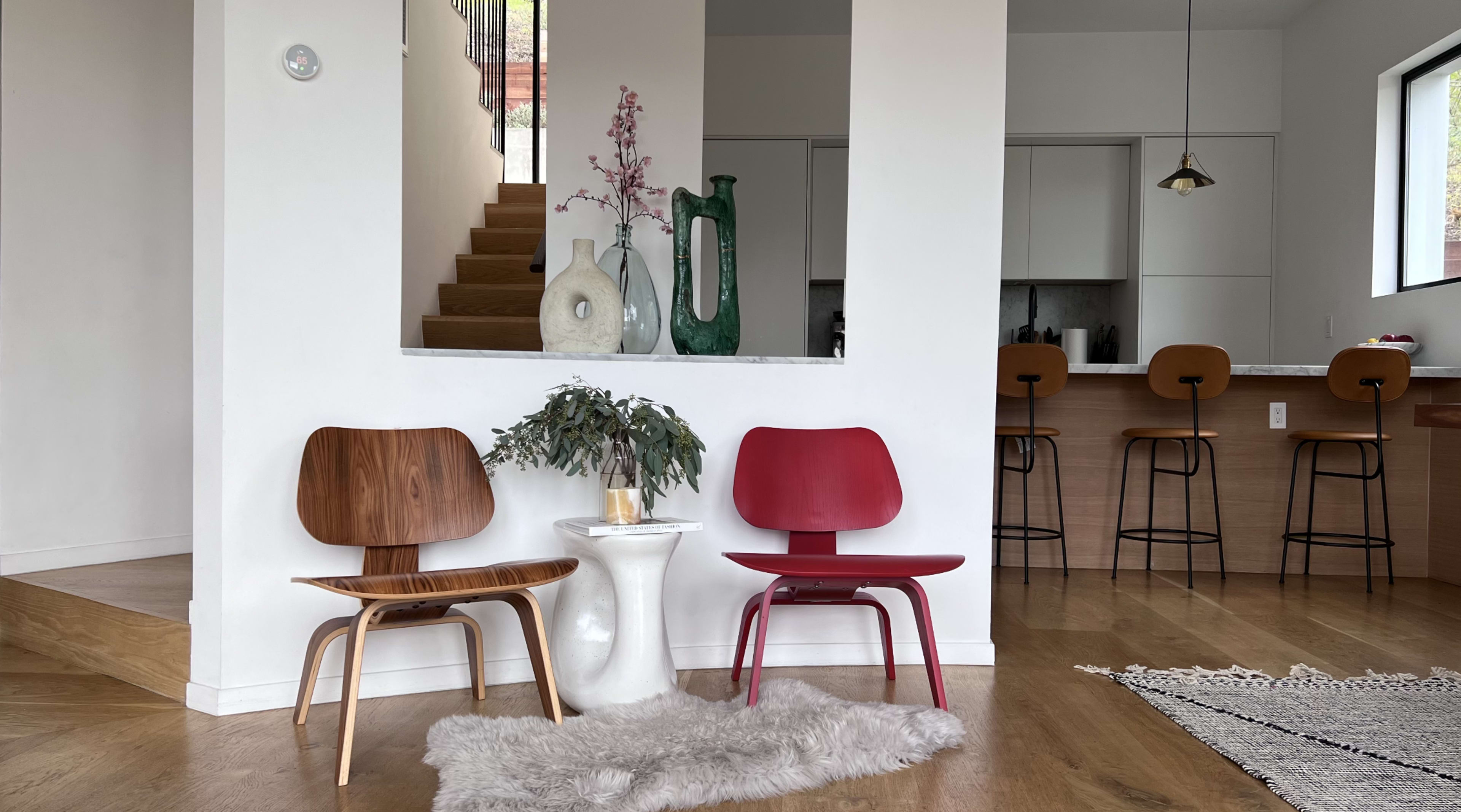 A modern living space features two chairs, a small table, and a staircase leading to an upper level, with a kitchen in the background.