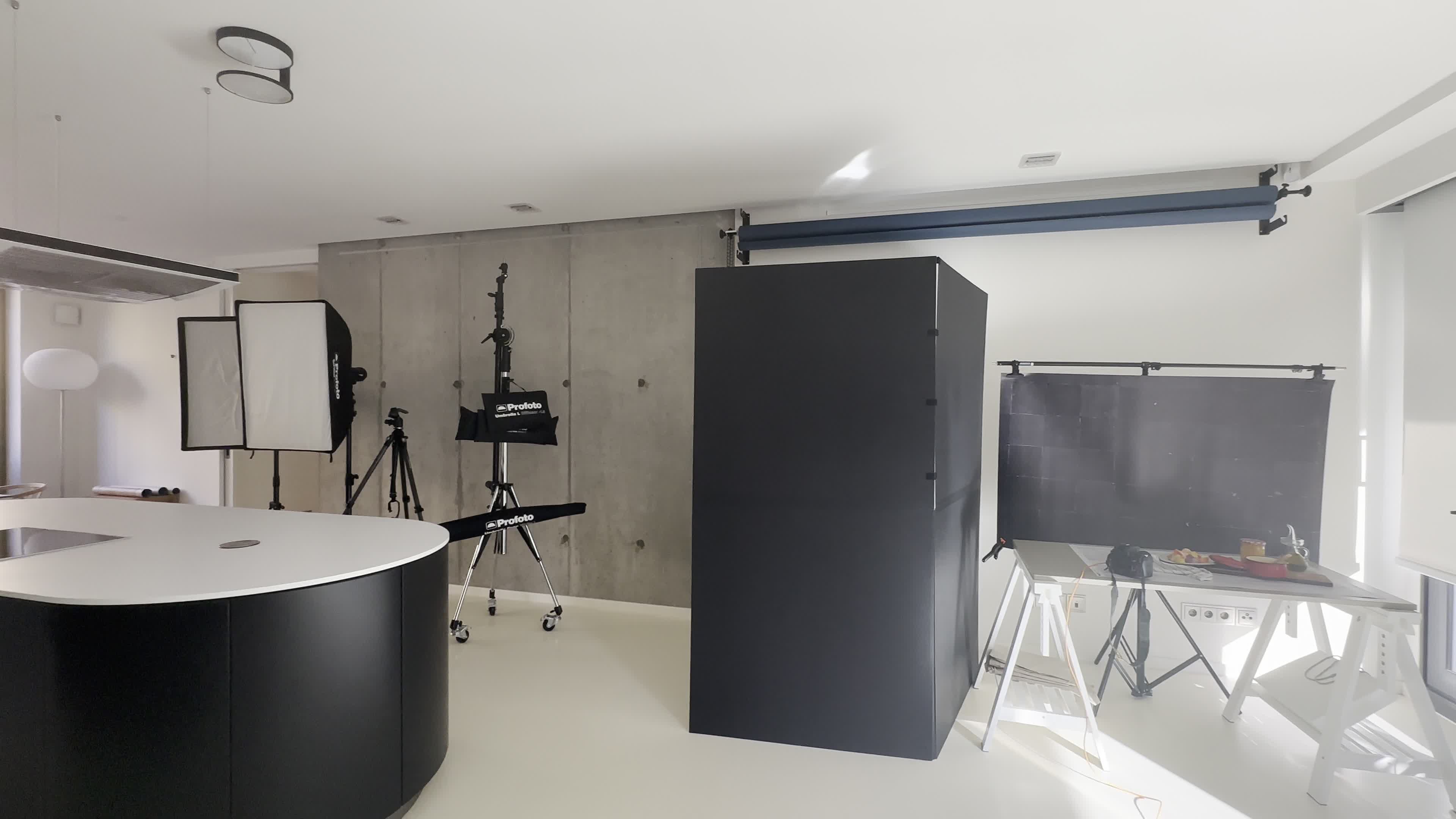 A modern photography studio featuring a black backdrop, lighting equipment, a white circular table, and a clean, minimalist design.