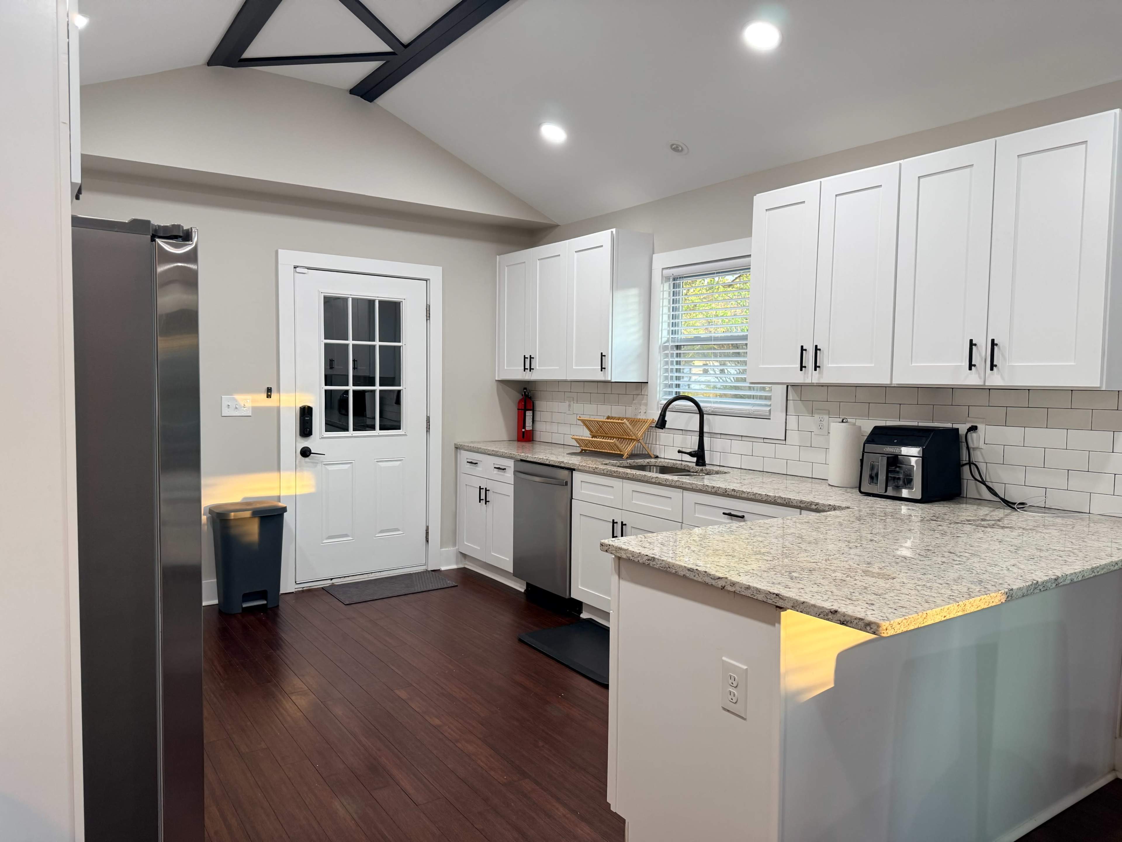 The image shows a modern kitchen featuring white cabinetry, stainless steel appliances, a granite countertop, and a door leading to an outdoor area.