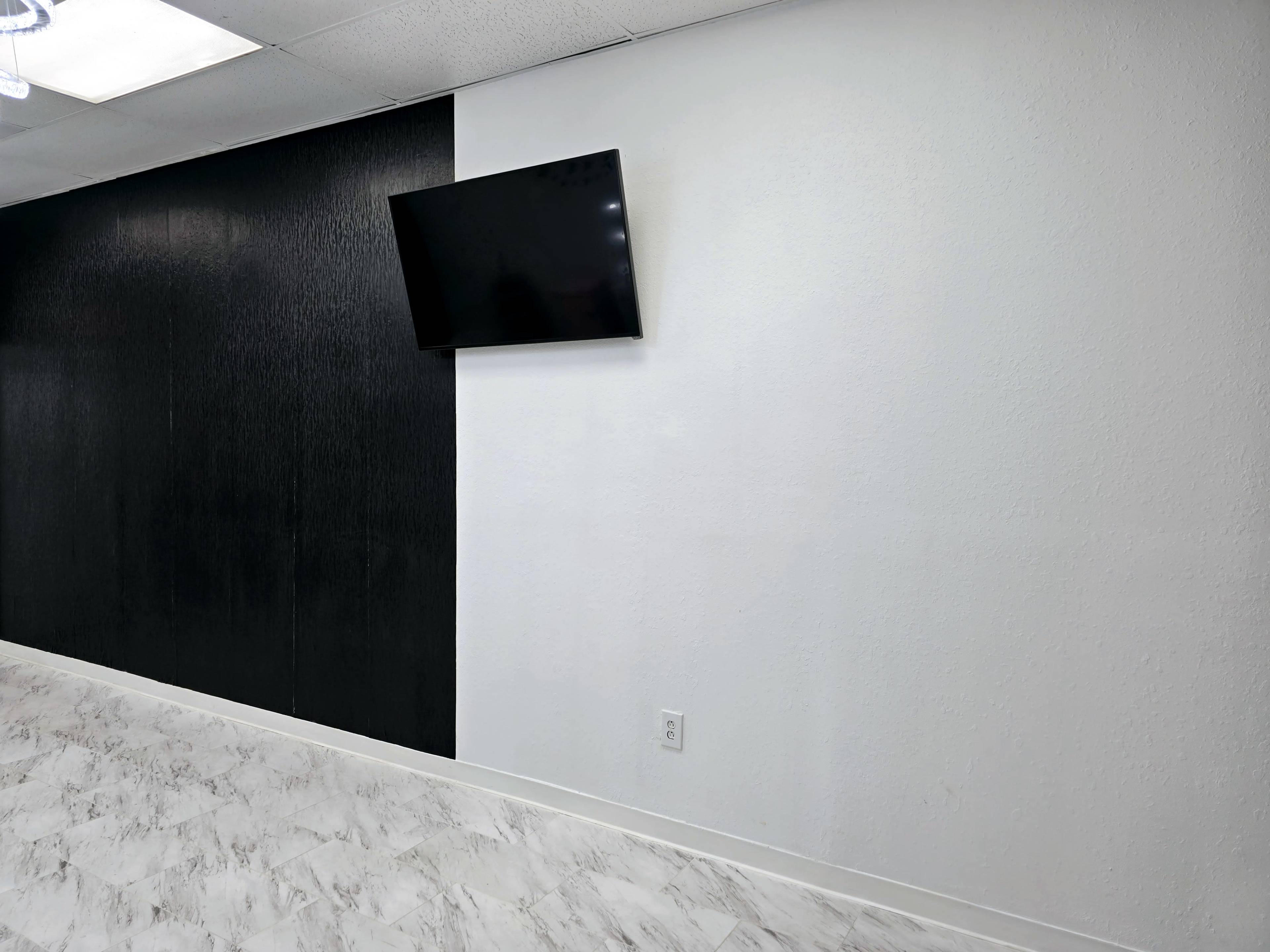 A room with a black wall on one side, a white wall on the other, and a flat-screen television mounted on the white wall.