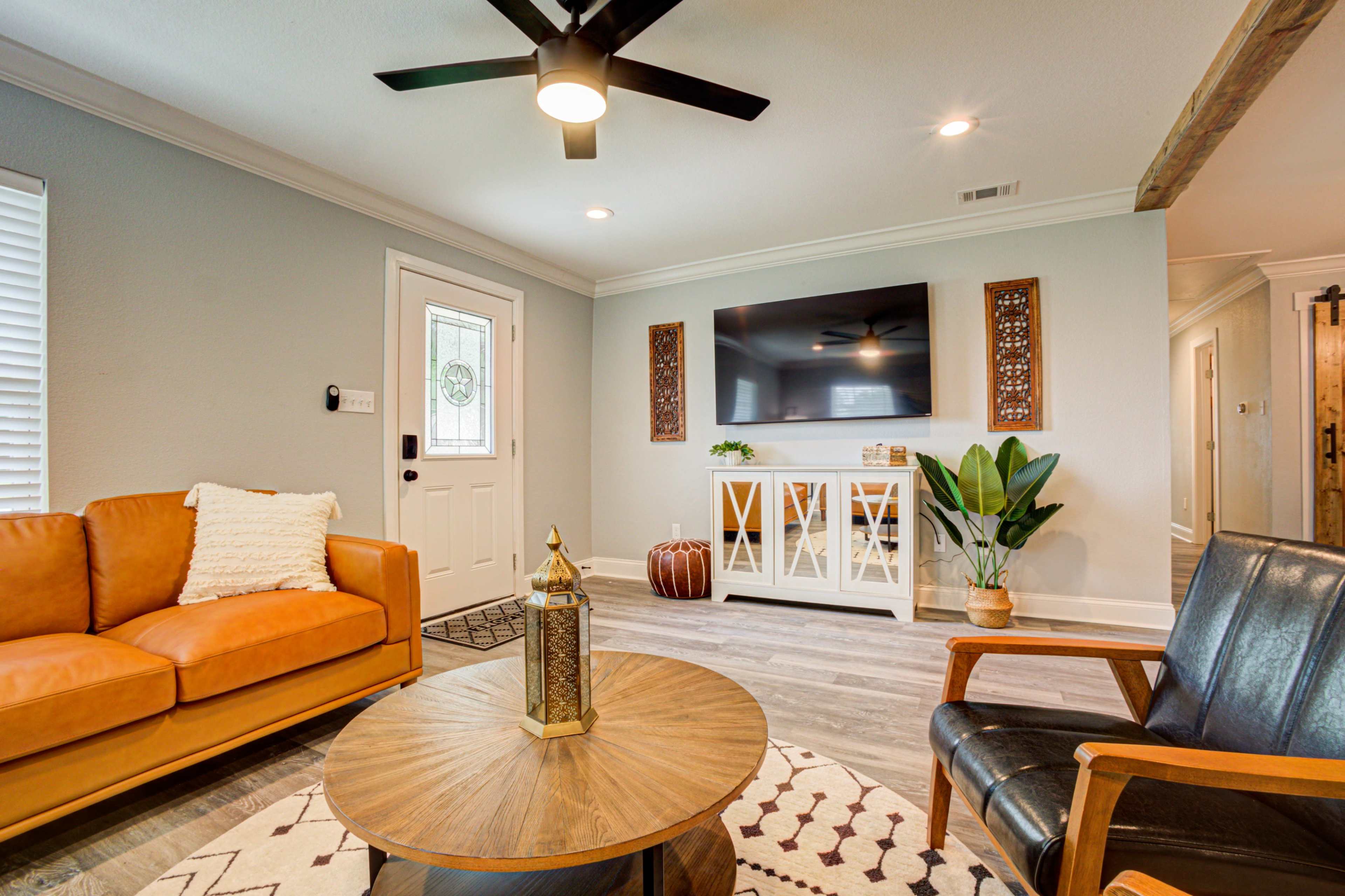 A modern living room featuring an orange leather sofa, a black armchair, a round wooden coffee table, a television mounted on the wall, and a potted plant.