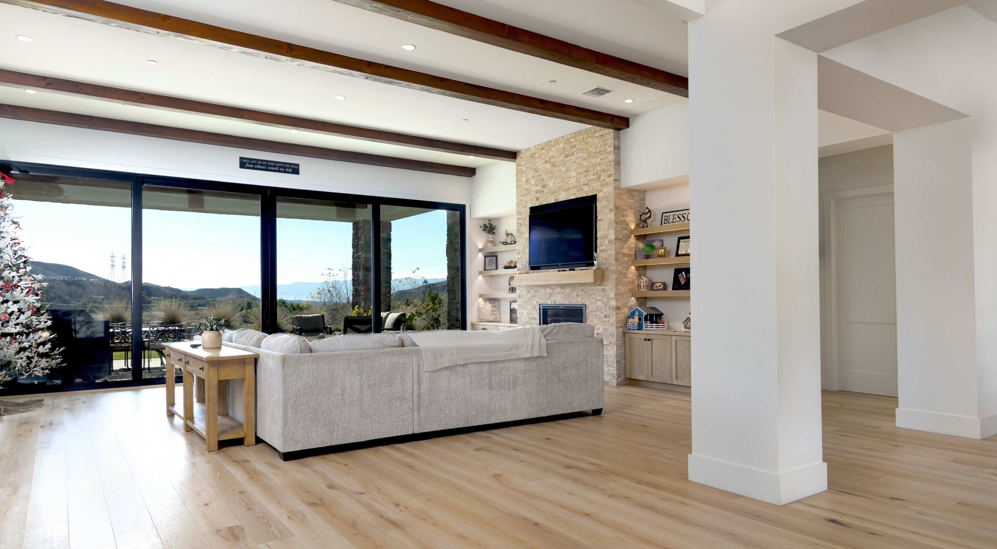A spacious living room features a light-colored sofa, a stone fireplace, and large windows showcasing a view of the outdoors.