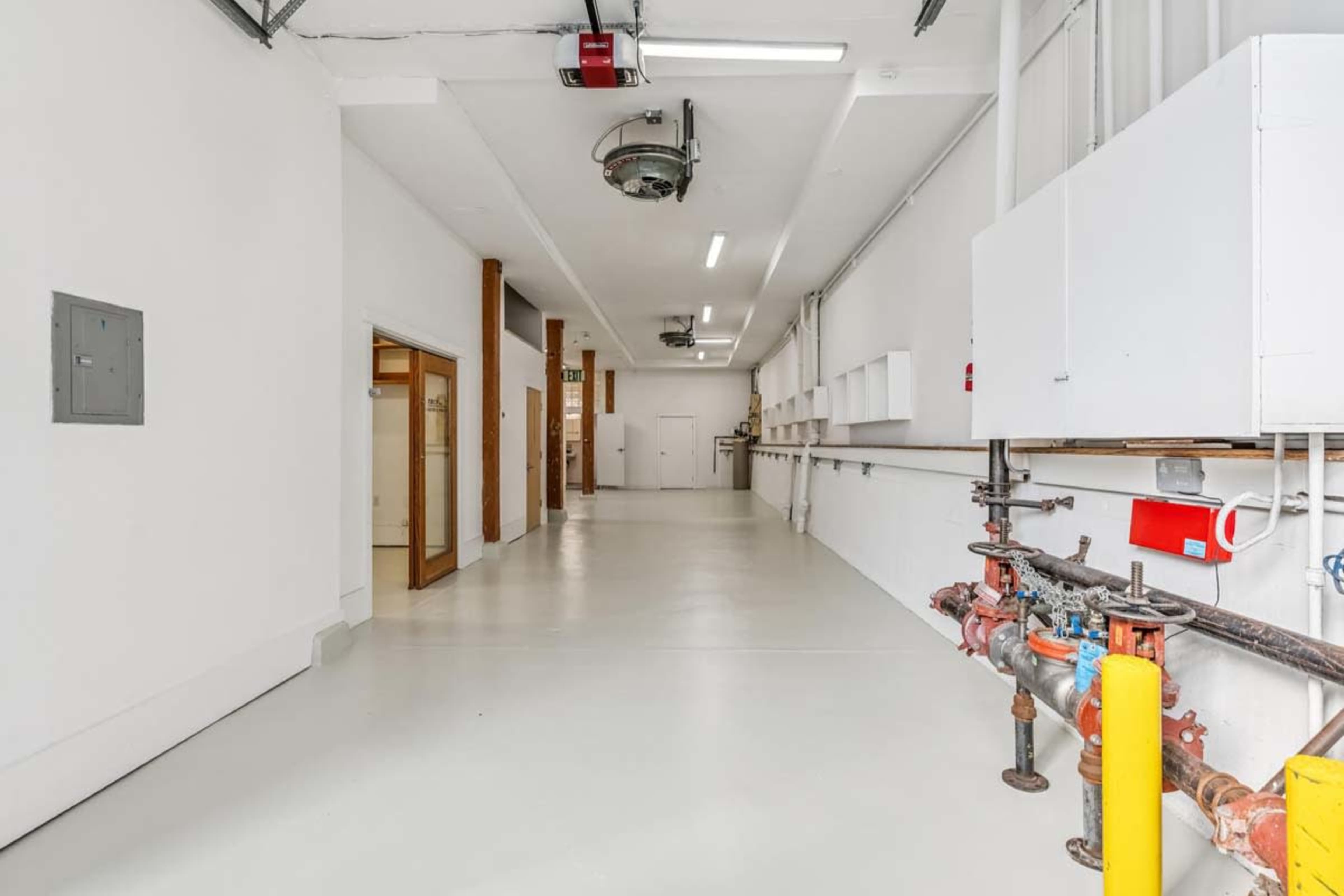 The image shows a long, well-lit corridor with white walls, a smooth floor, and utility equipment along one side.