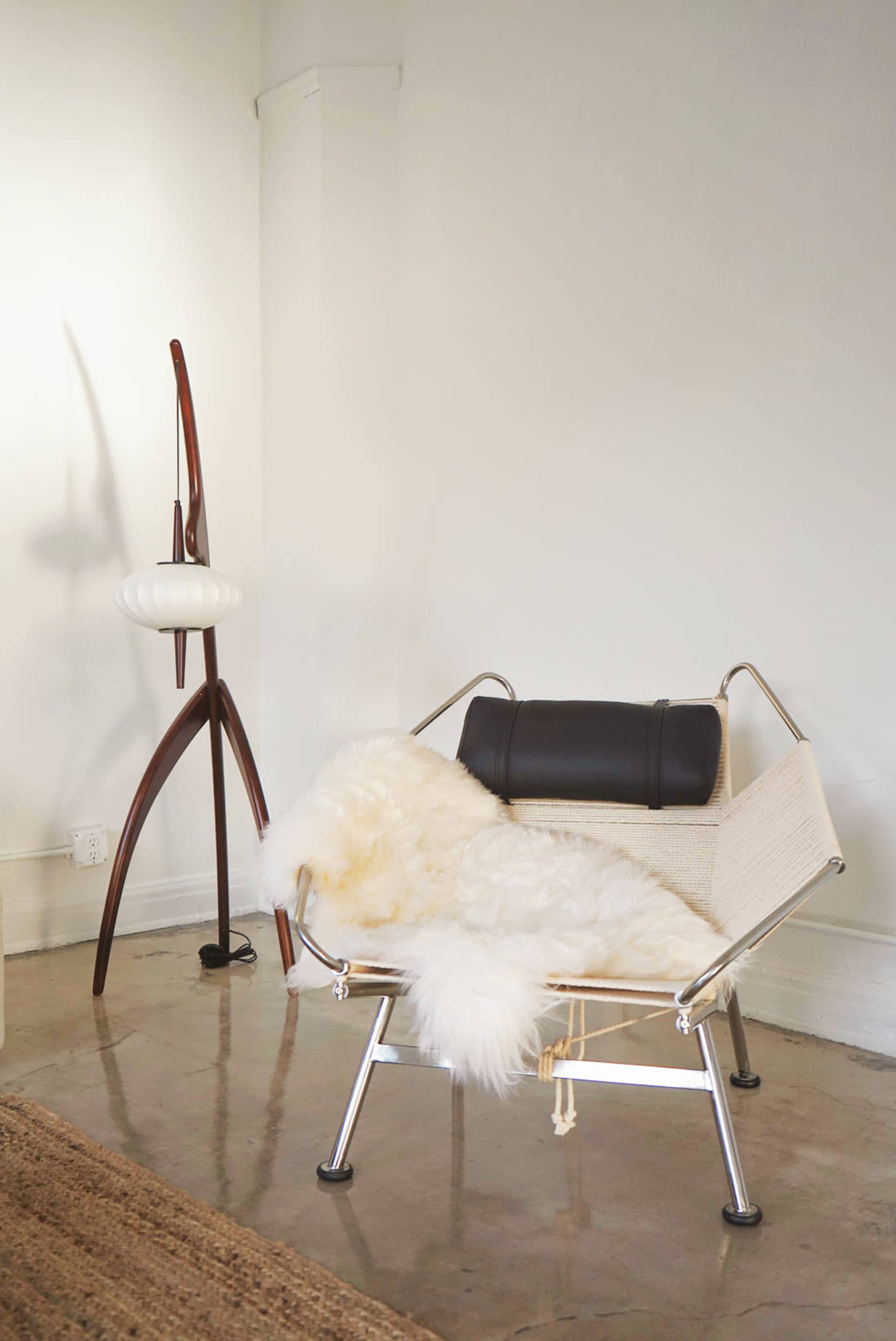 A minimalist seating area featuring a modern chair with a white fur throw and a wooden lamp beside it.