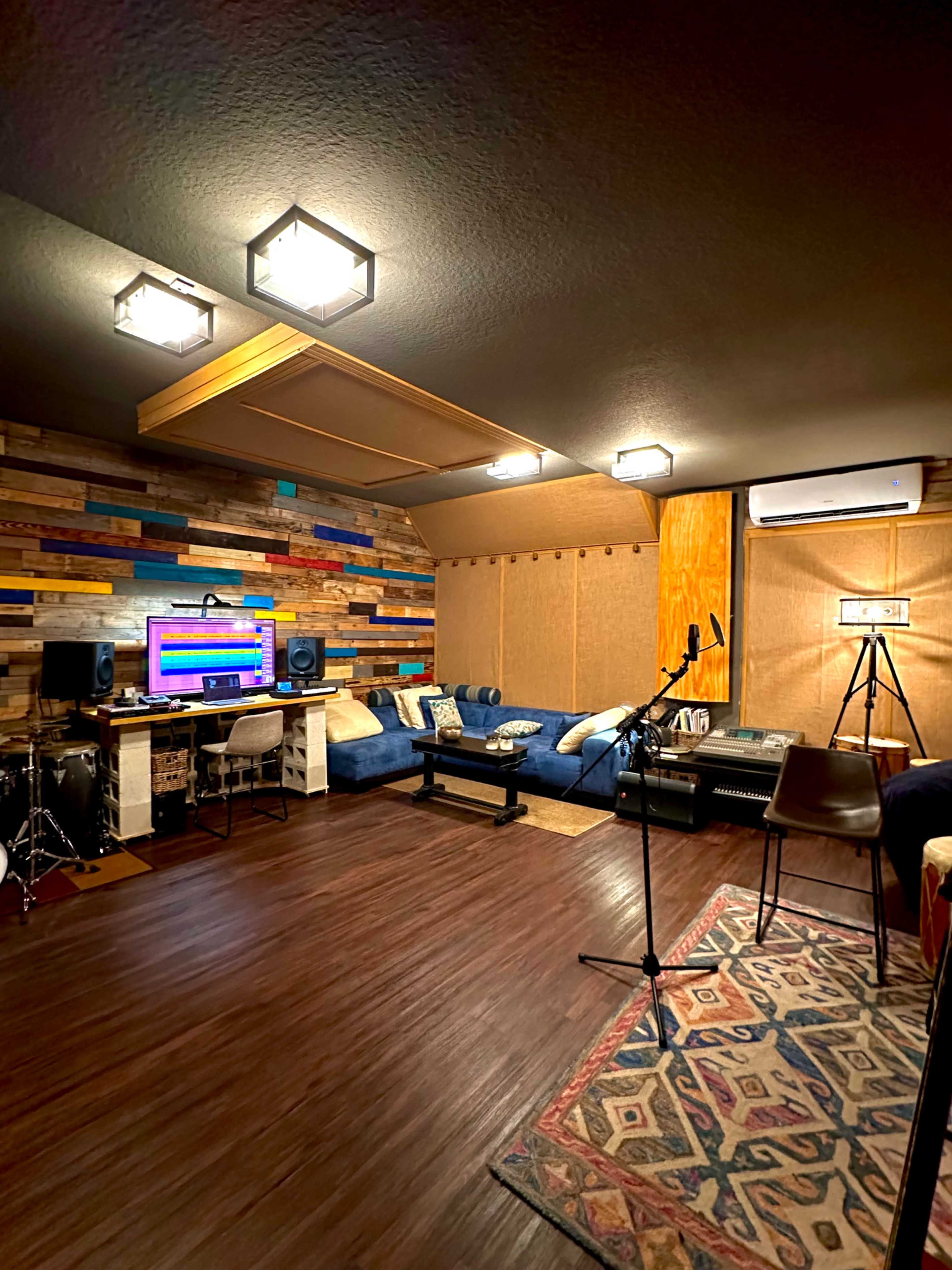 A recording studio featuring a mix of colorful wooden panels, comfortable seating, musical instruments, and professional audio equipment.