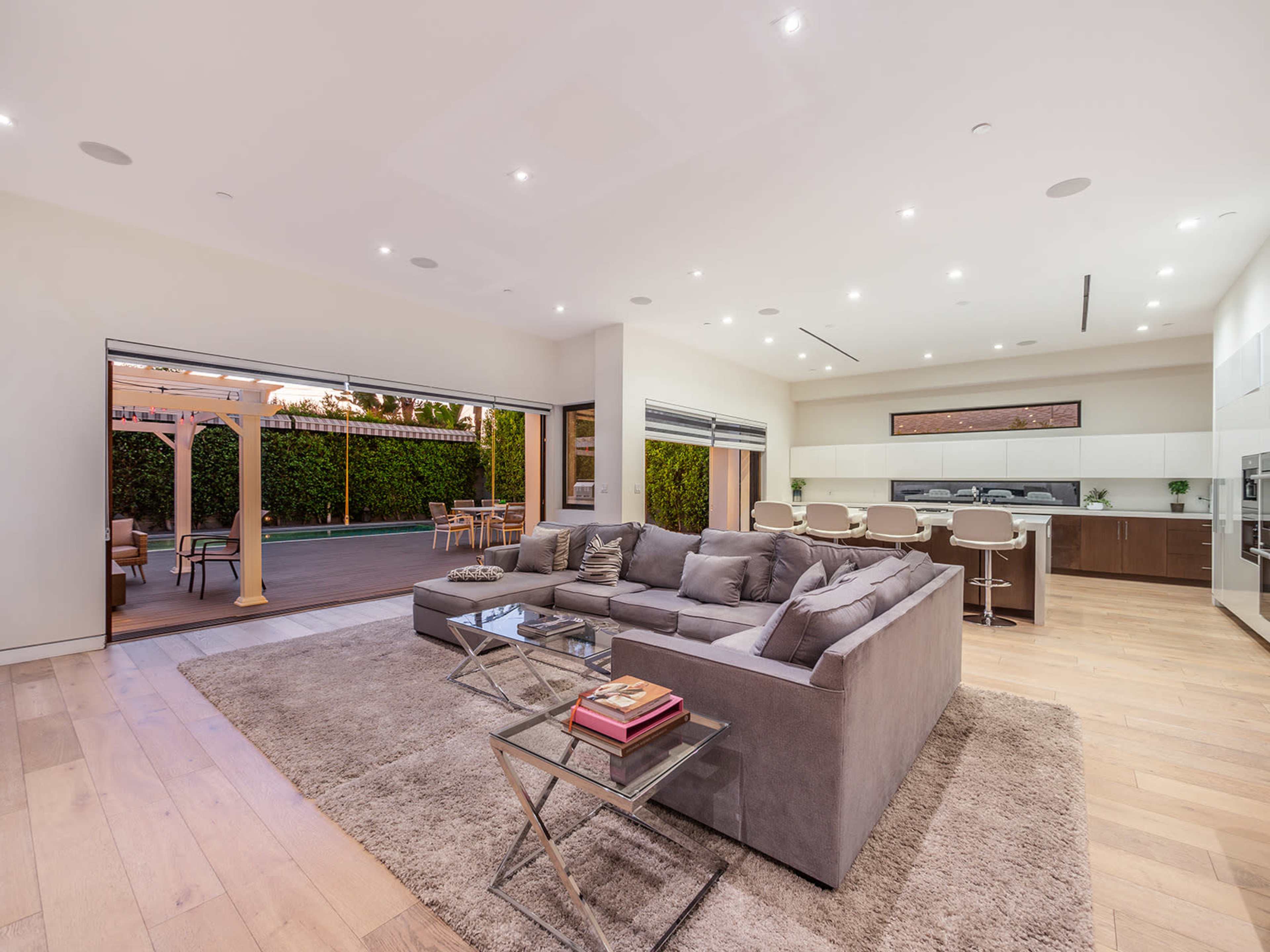 A modern living room features a gray sectional sofa and a glass-top coffee table, with large sliding doors opening to an outdoor patio area.