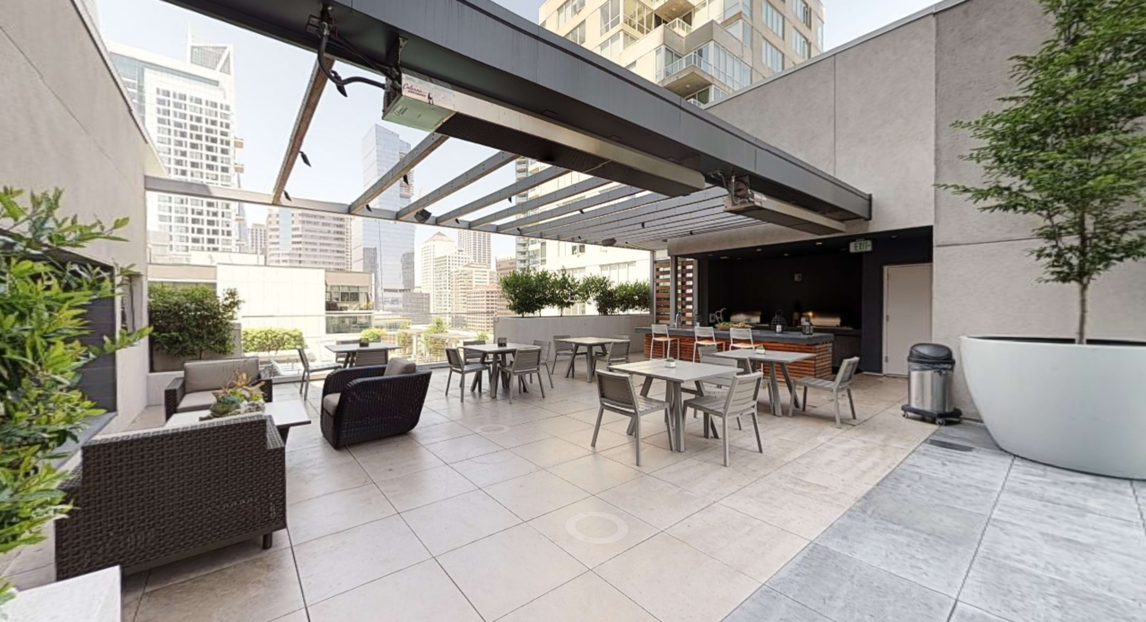 A rooftop terrace with outdoor seating, tables, and a view of surrounding buildings.