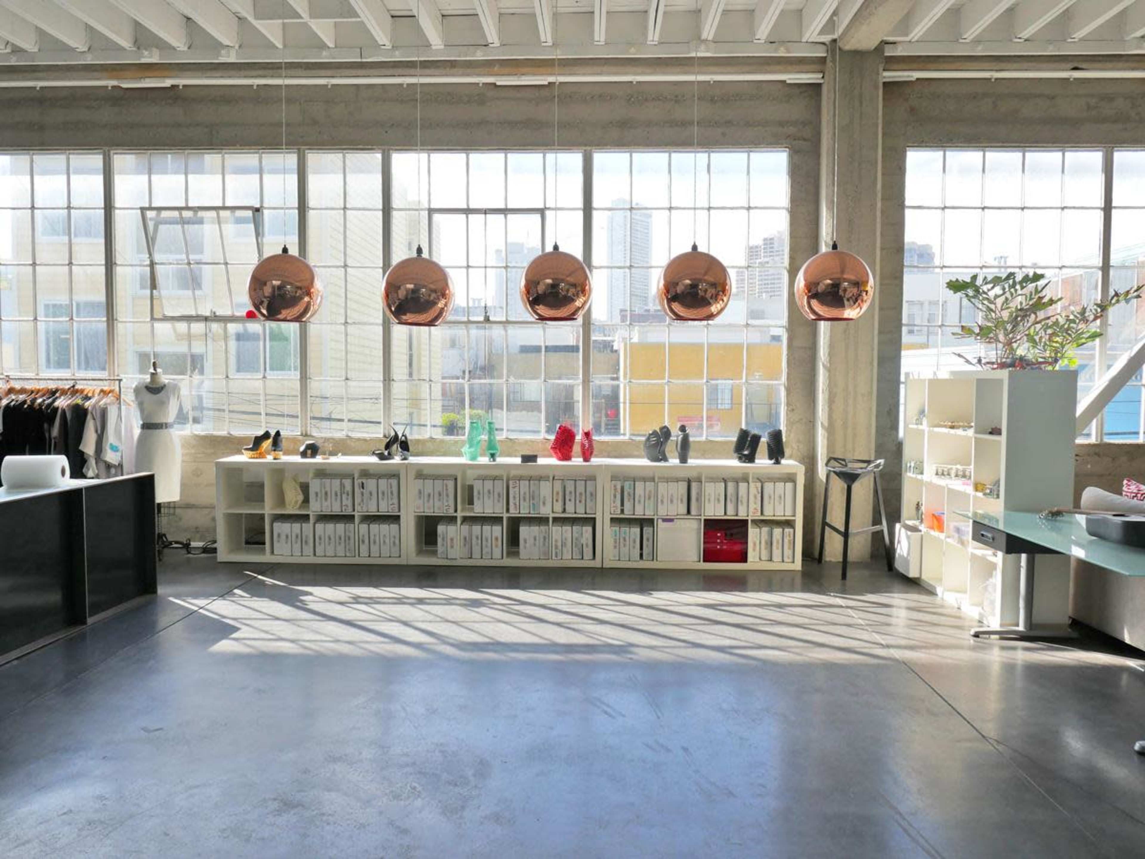 A spacious interior with large windows, displaying a collection of copper pendant lights, shelves of shoes, and a minimalist display area.