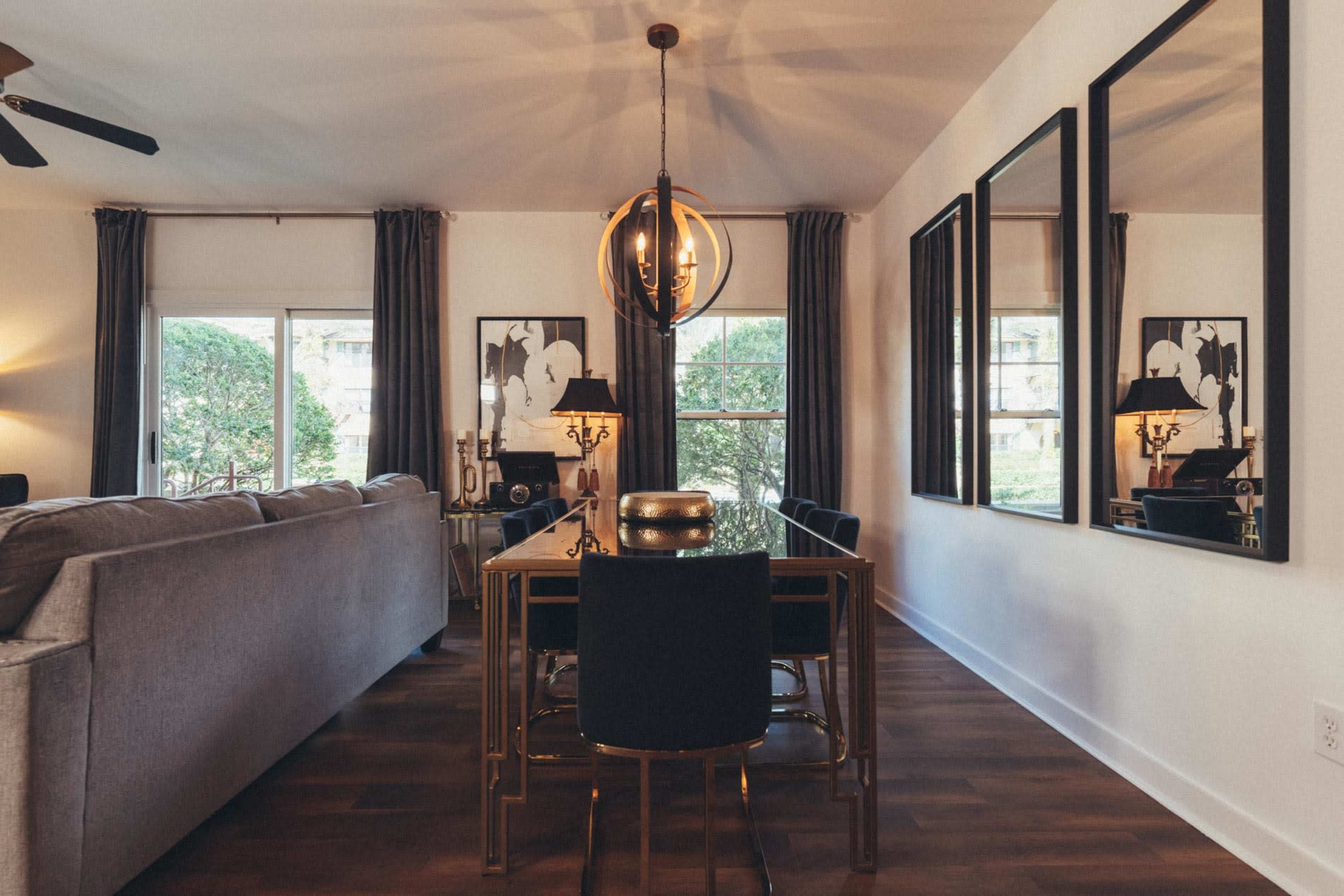 A dining area with a wooden table surrounded by black chairs, featuring a modern pendant light and large mirrors on the wall.