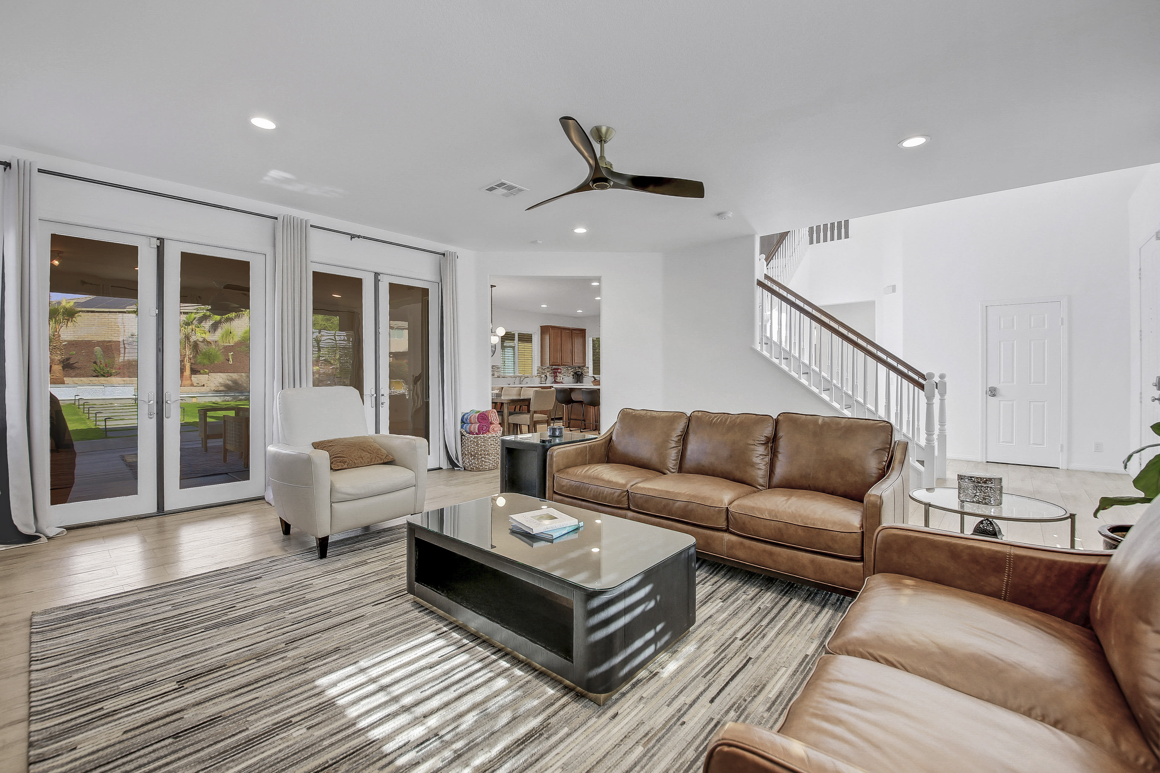 The living room features brown leather sofas, a coffee table, and large sliding glass doors leading to an outdoor area.